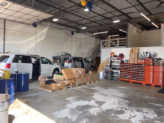 Large indoor workshop with cars, pallets of boxes, and red tool cabinets.