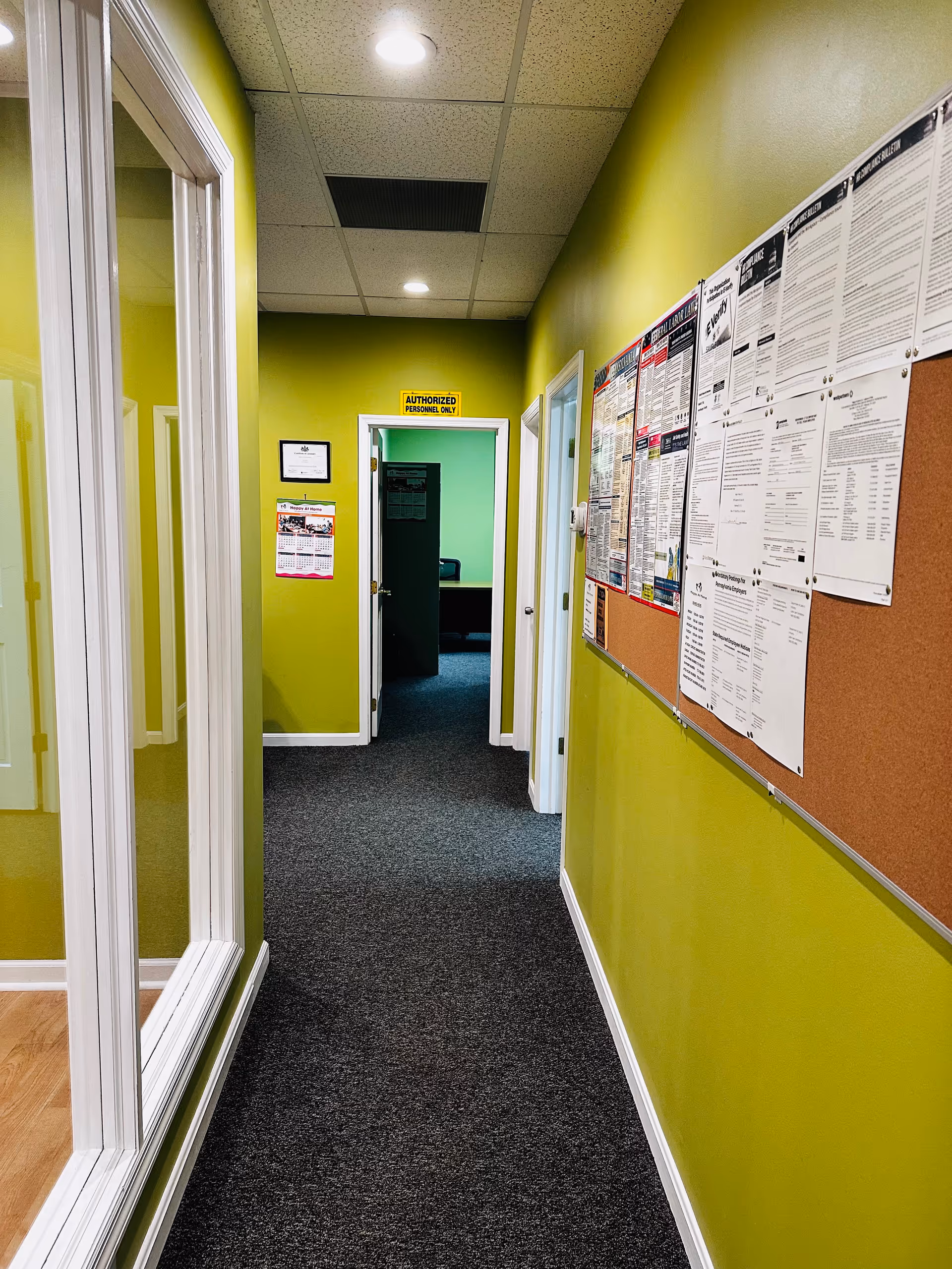 Bright lime-green hallway with a corkboard, glass-walled room, and doors.