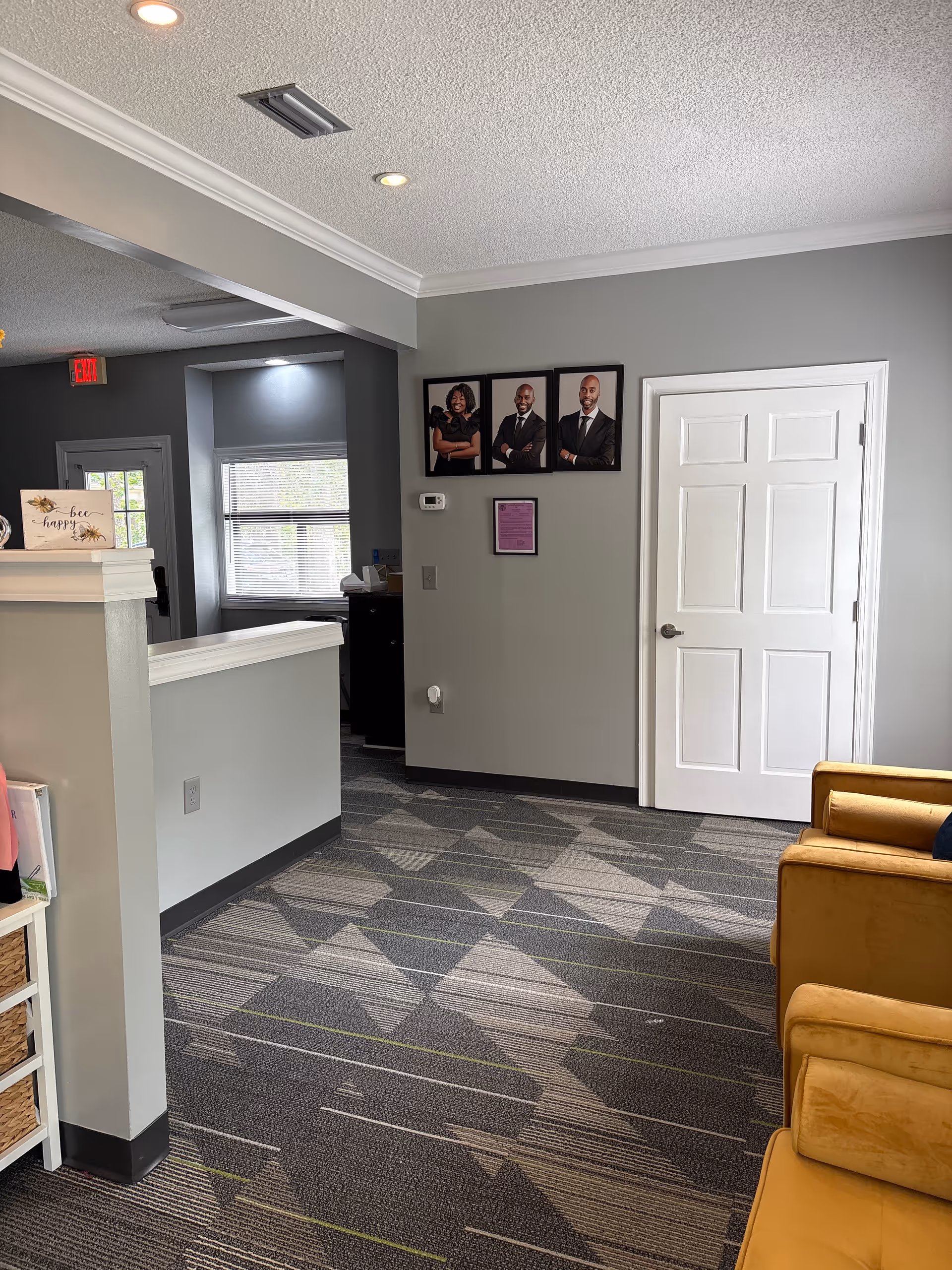Interior reception area with a front desk, framed portraits, and mustard seating.