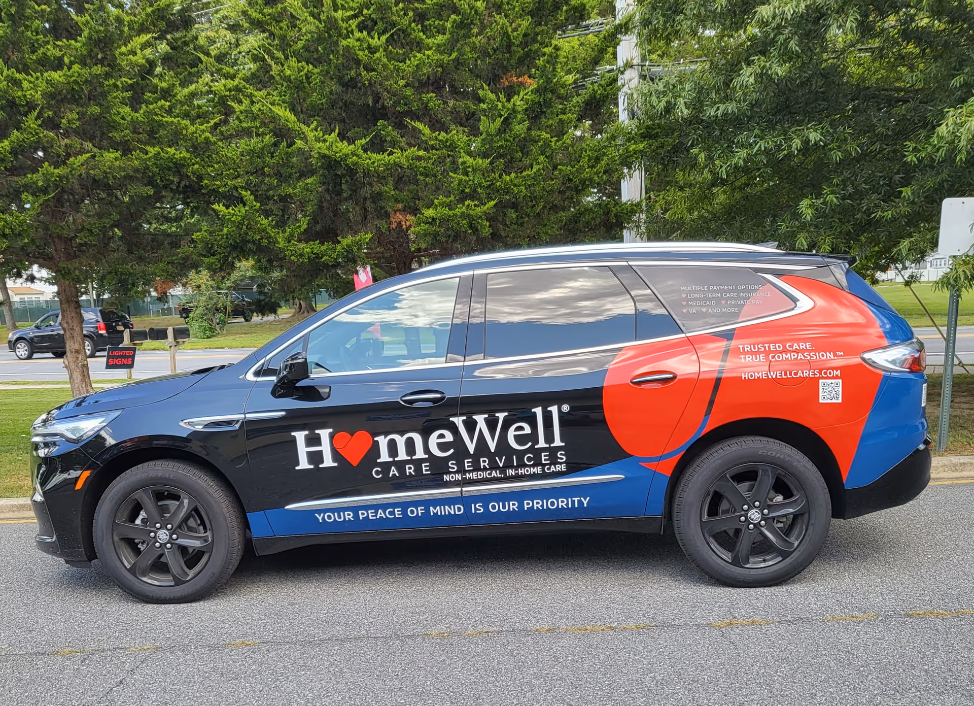 Branded HomeWell Care Services vehicle parked on a street with trees.
