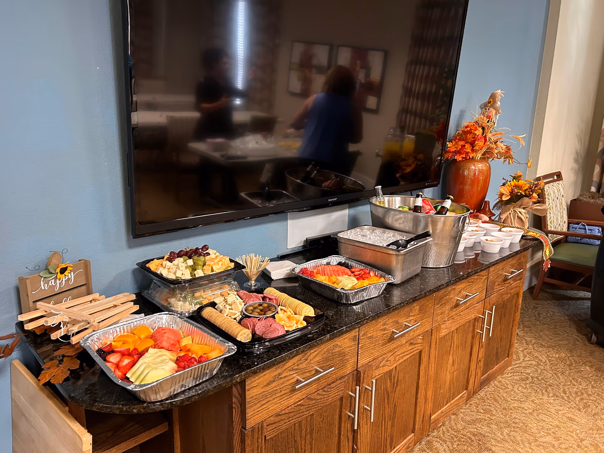 Buffet-style snack spread on a dark counter beneath a wall-mounted TV.