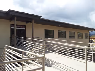 Exterior view of a single-story facility with a ramp and metal railing leading to the entrance