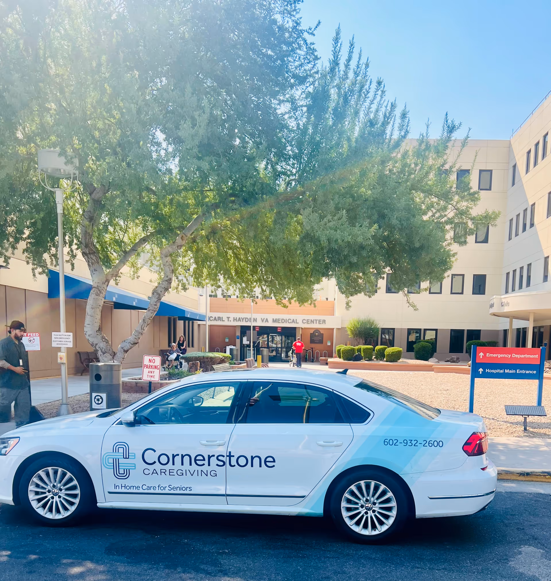 A white Cornerstone Caregiving car parked outside a medical center entrance.
