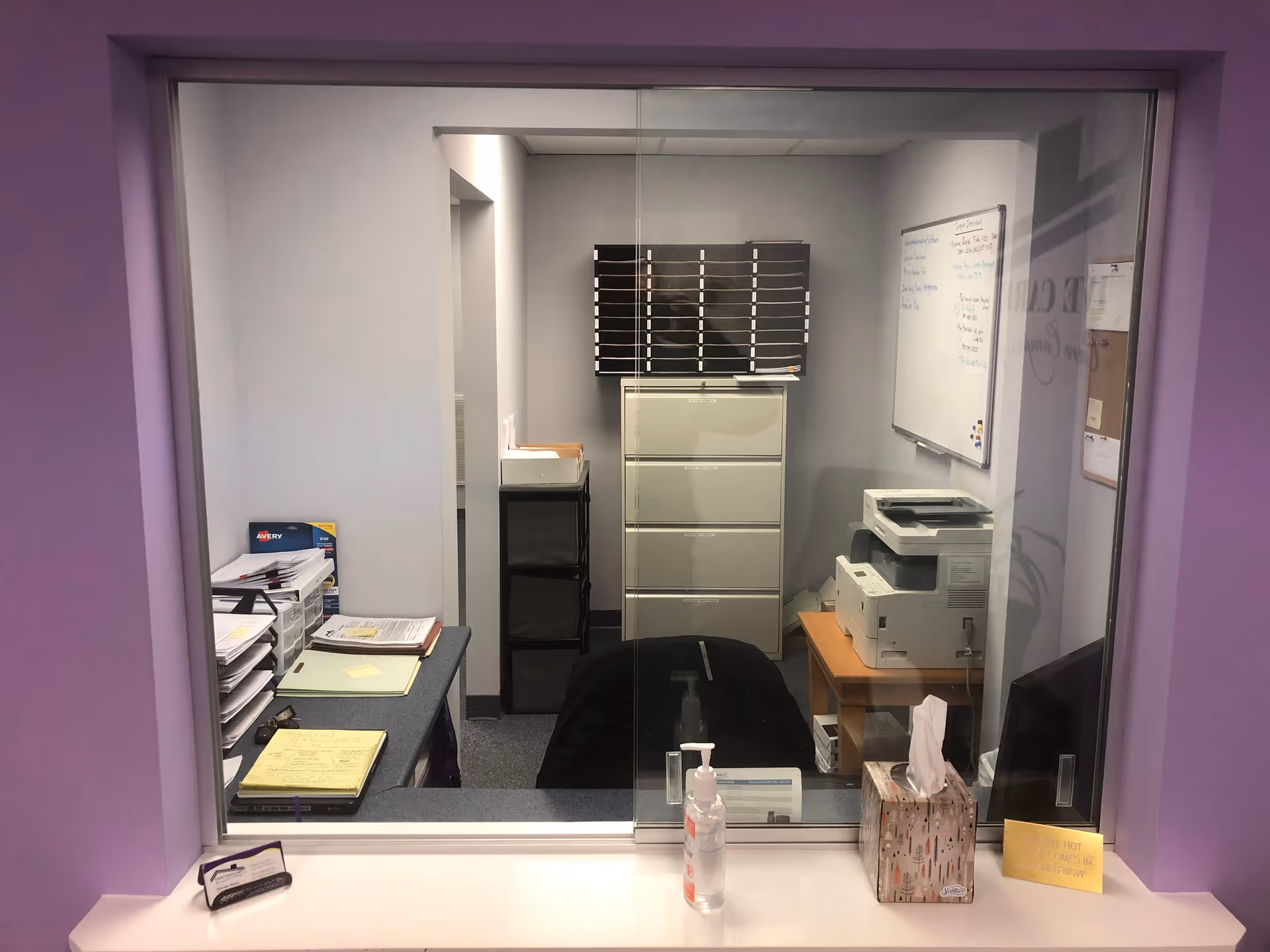 Glass-walled office space with mailboxes, a printer, filing cabinets, and sanitizer.