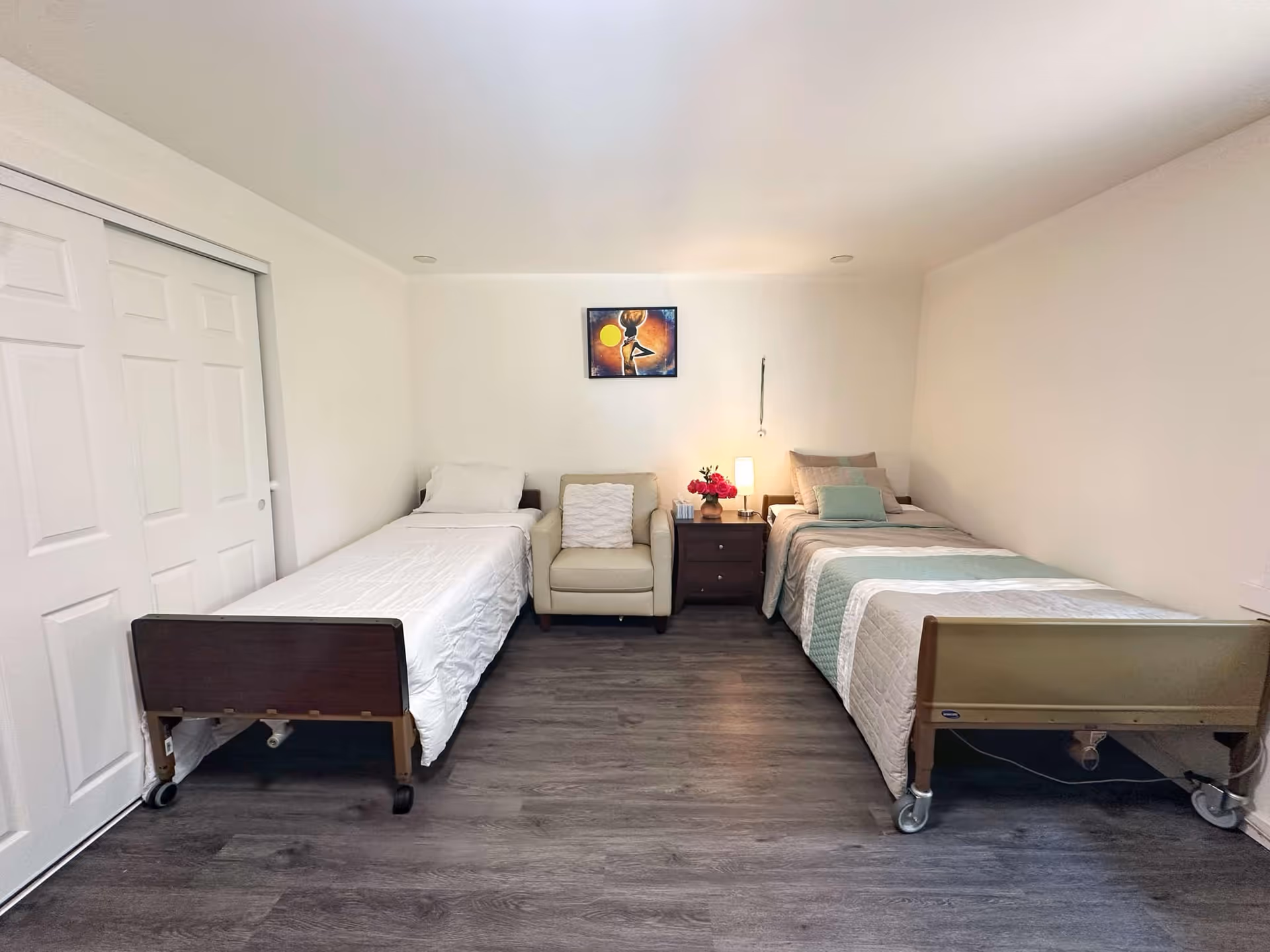 Two beds with a nightstand and chair in a clean, bright shared bedroom.
