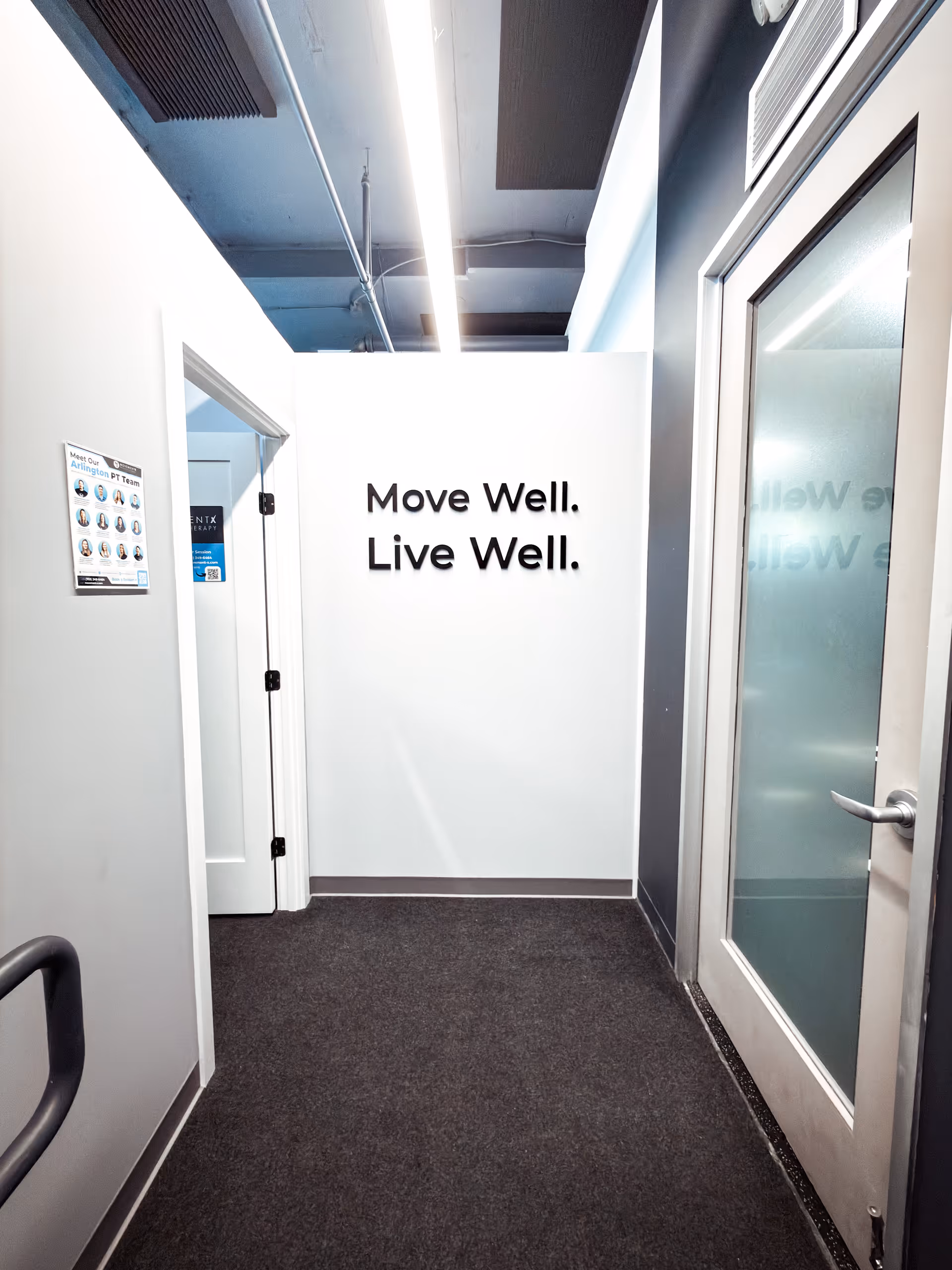 A white-walled hallway inside MovementX Physical Therapy in Arlington with a 'Move Well. Live Well.' sign.