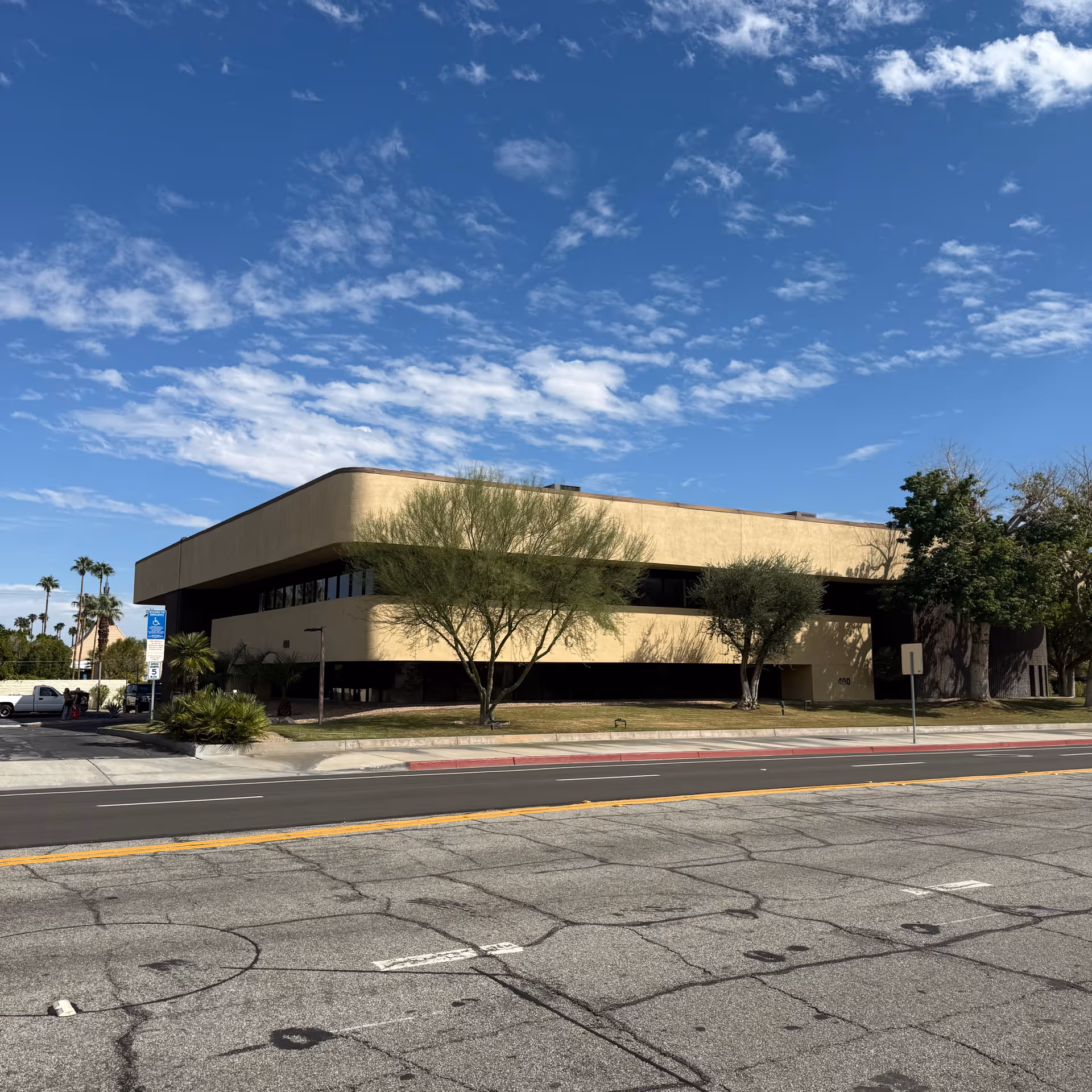 Beige modern building along a street with trees and a clear blue sky