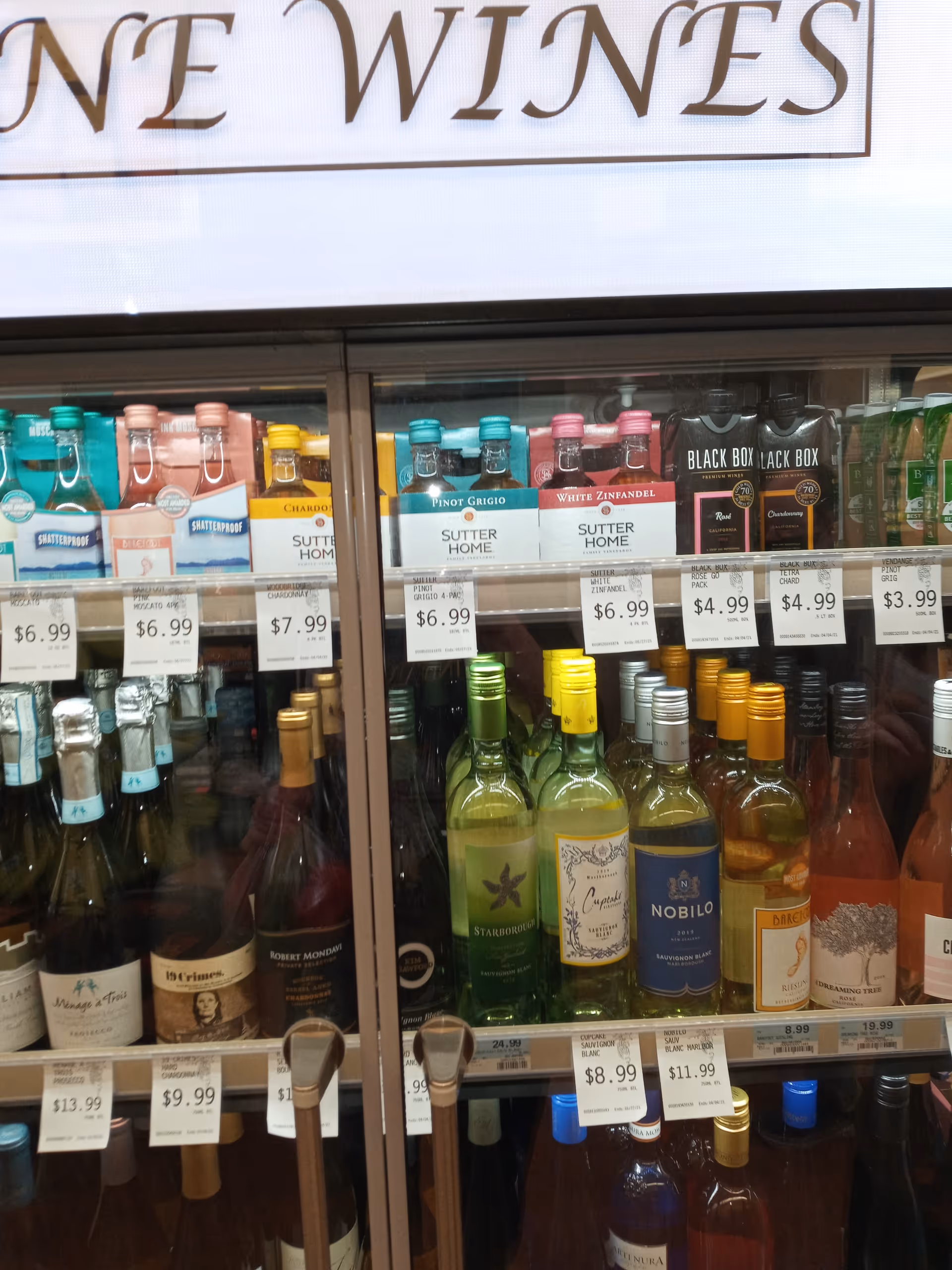 Wine bottles displayed behind glass with price tags in a Discount Drug Mart interior
