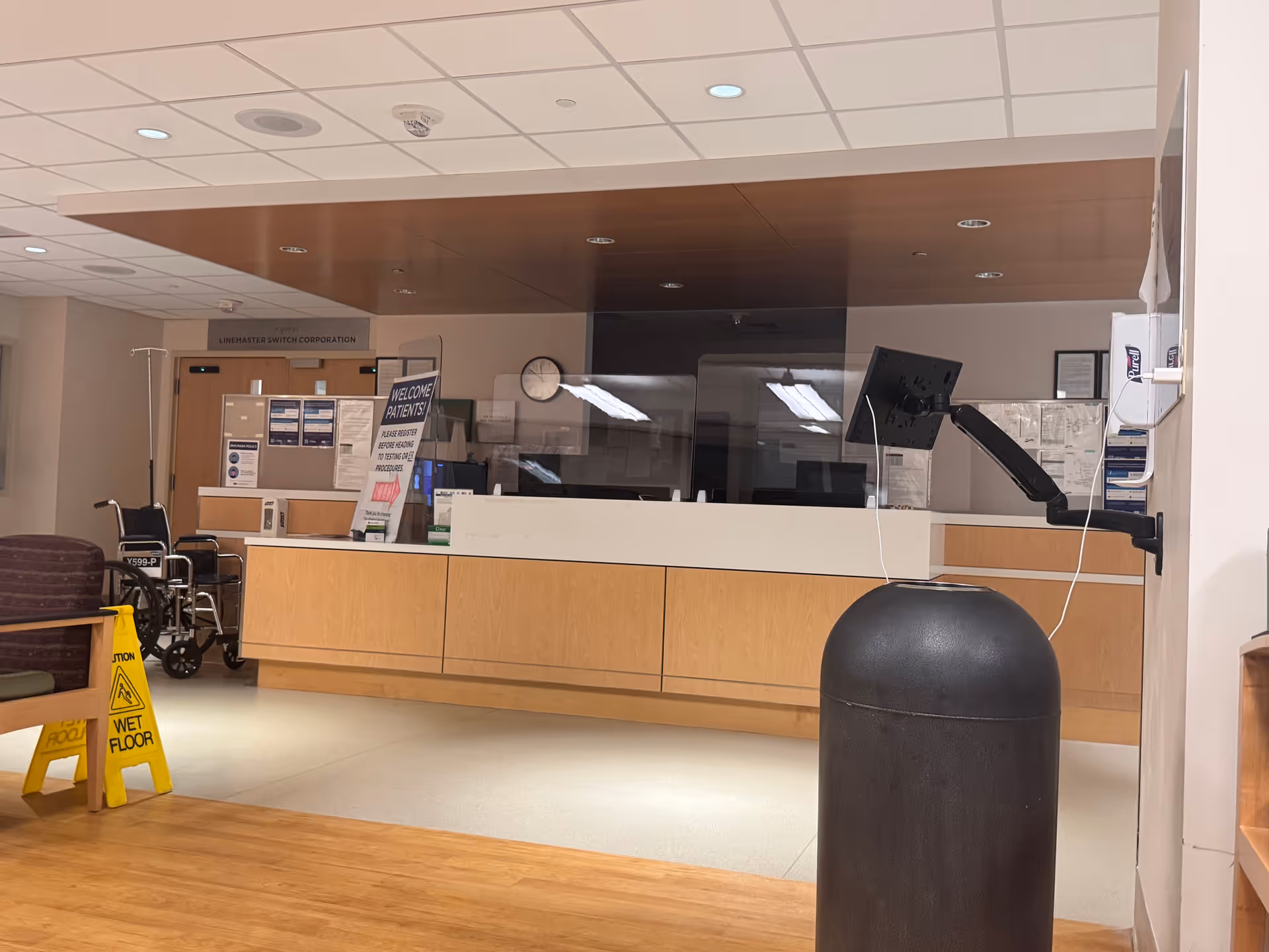 Lobby reception area with a long desk, signs, chairs, wheelchair, and wet-floor sign