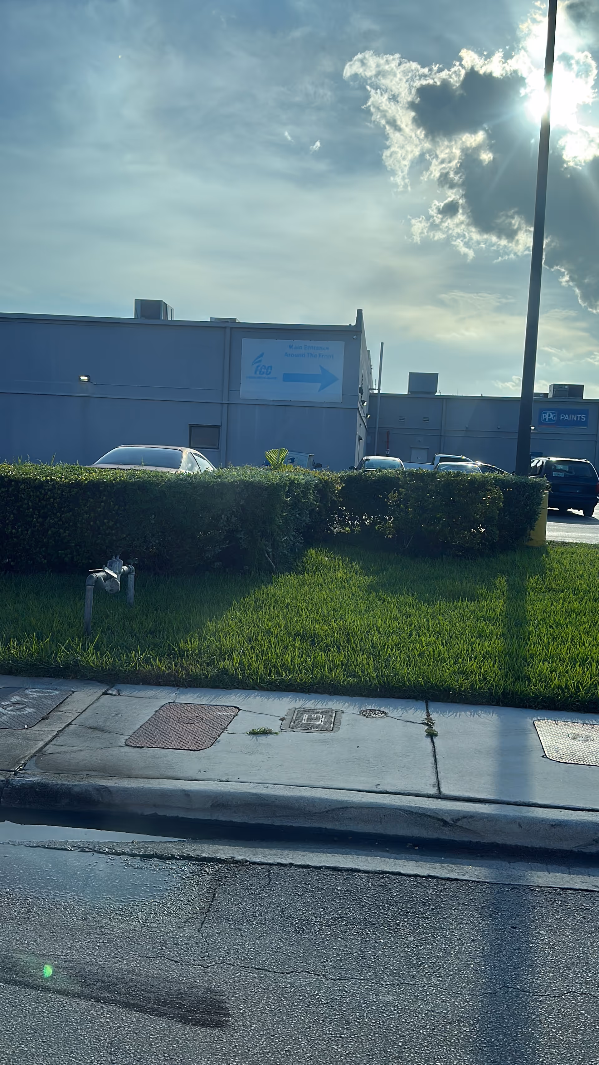 Exterior view of a commercial building with a hedge, sidewalk, and parked cars.
