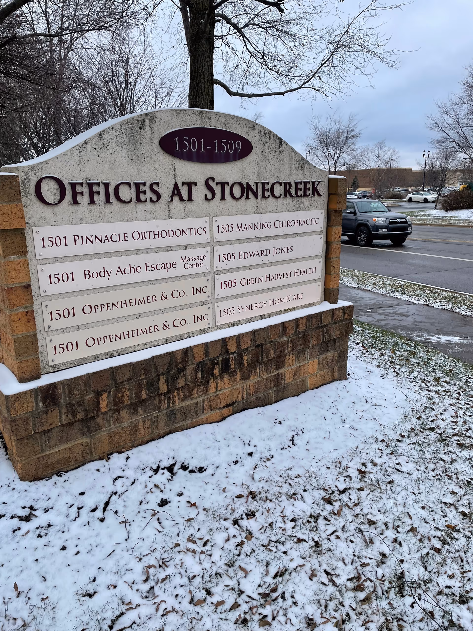 Outdoor stone sign for Offices at Stonecreek, including Synergy HomeCare, with snow on the ground.