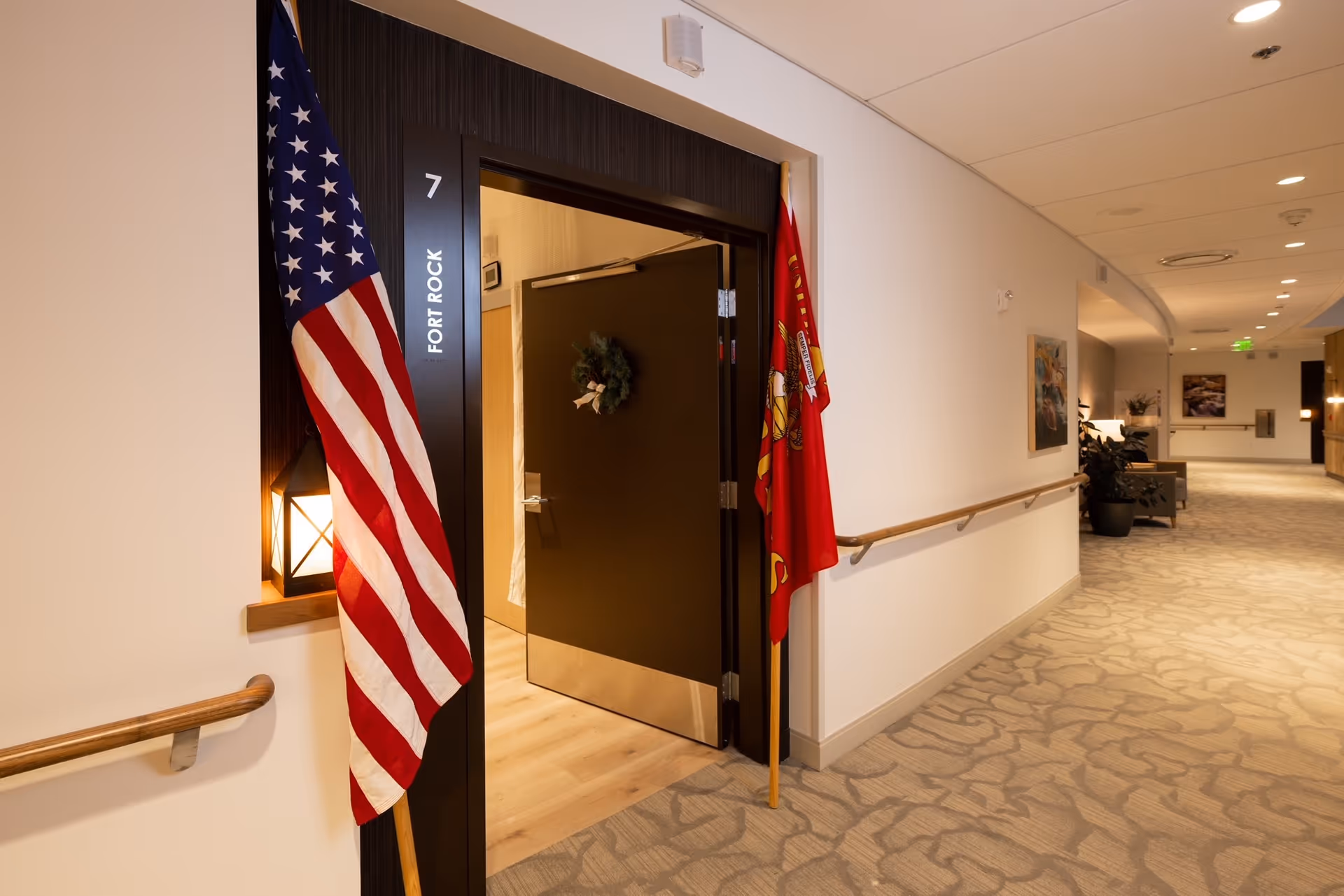 Interior corridor of a senior living facility with an open door and flags.