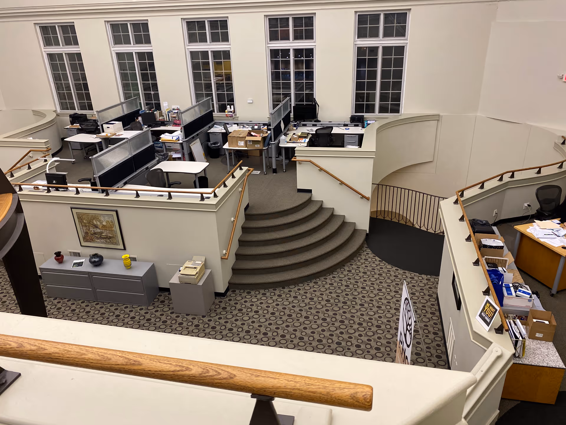 Two-story atrium with desks, cubicles, and a curved staircase in an office lobby.