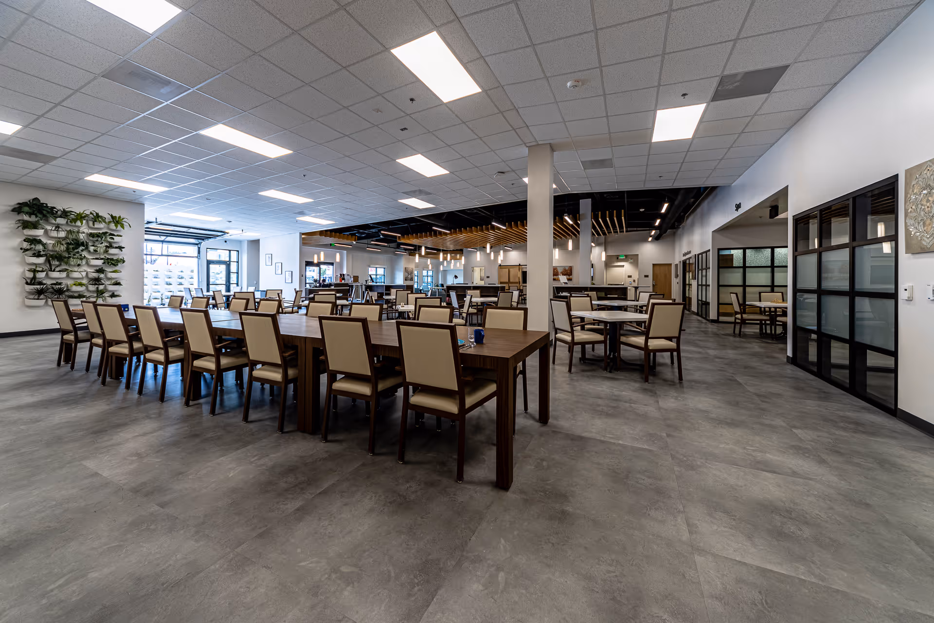 A spacious dining hall in a senior facility with long tables and beige chairs.