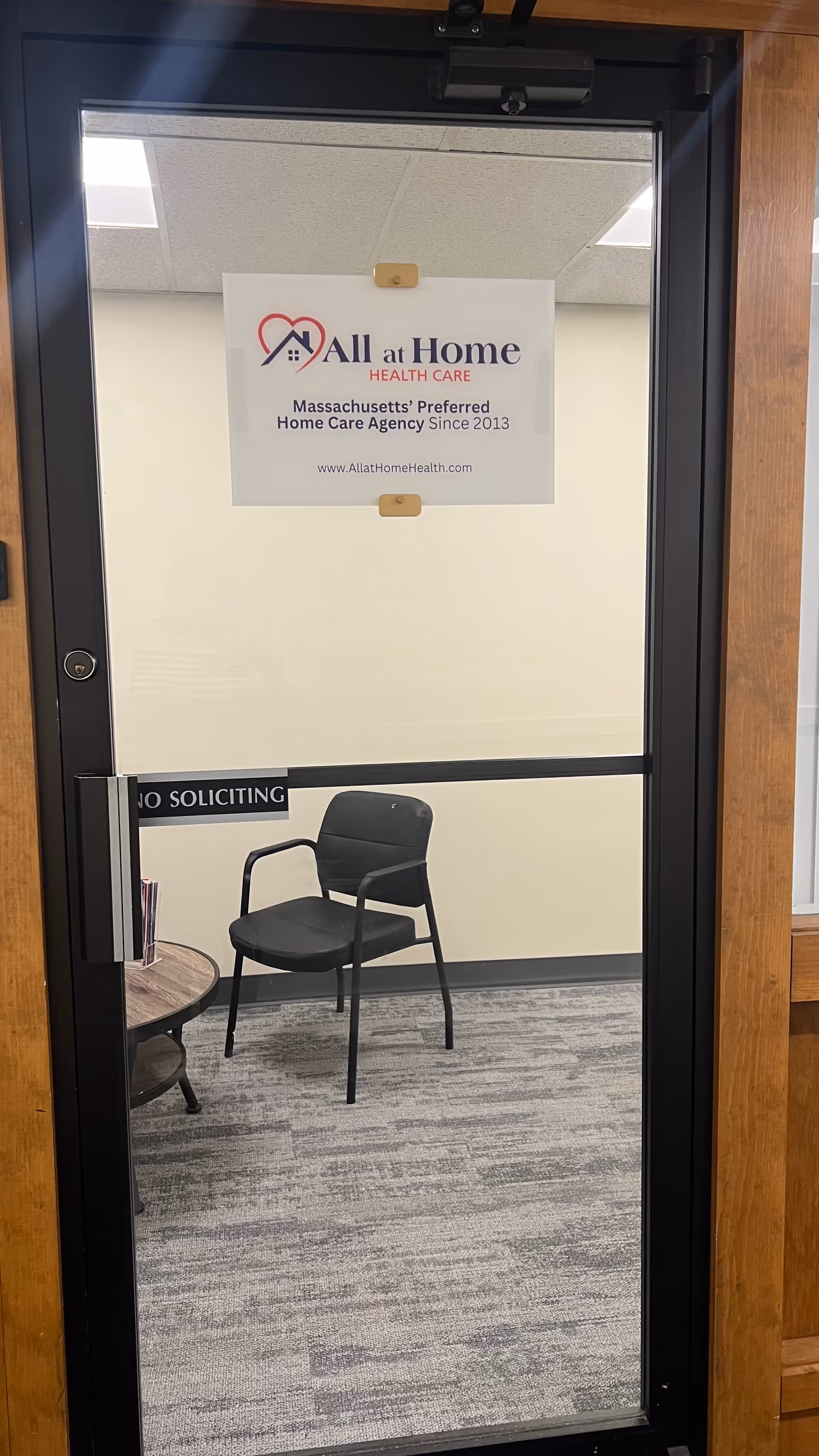 Interior office waiting area visible through a glass door, featuring a chair and sign.