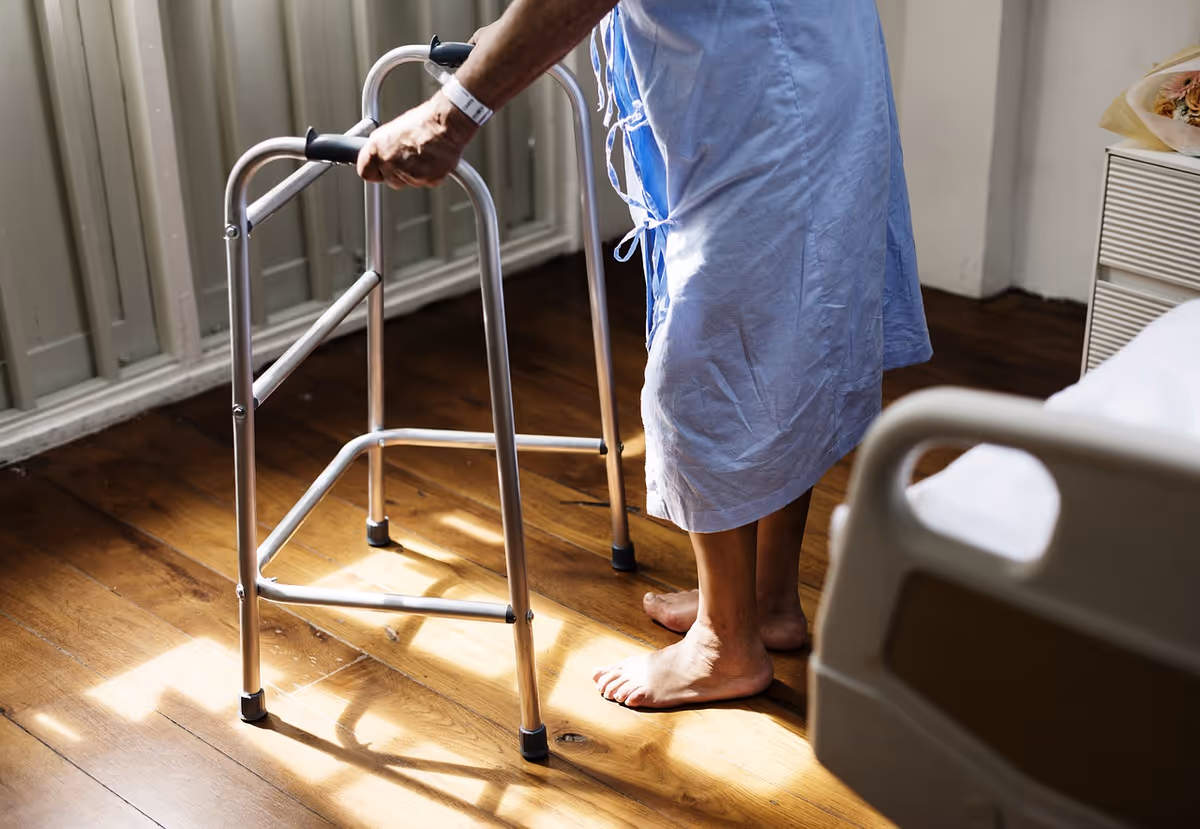 Resident's feet beside a walker in a sunlit bedroom beside a bed.