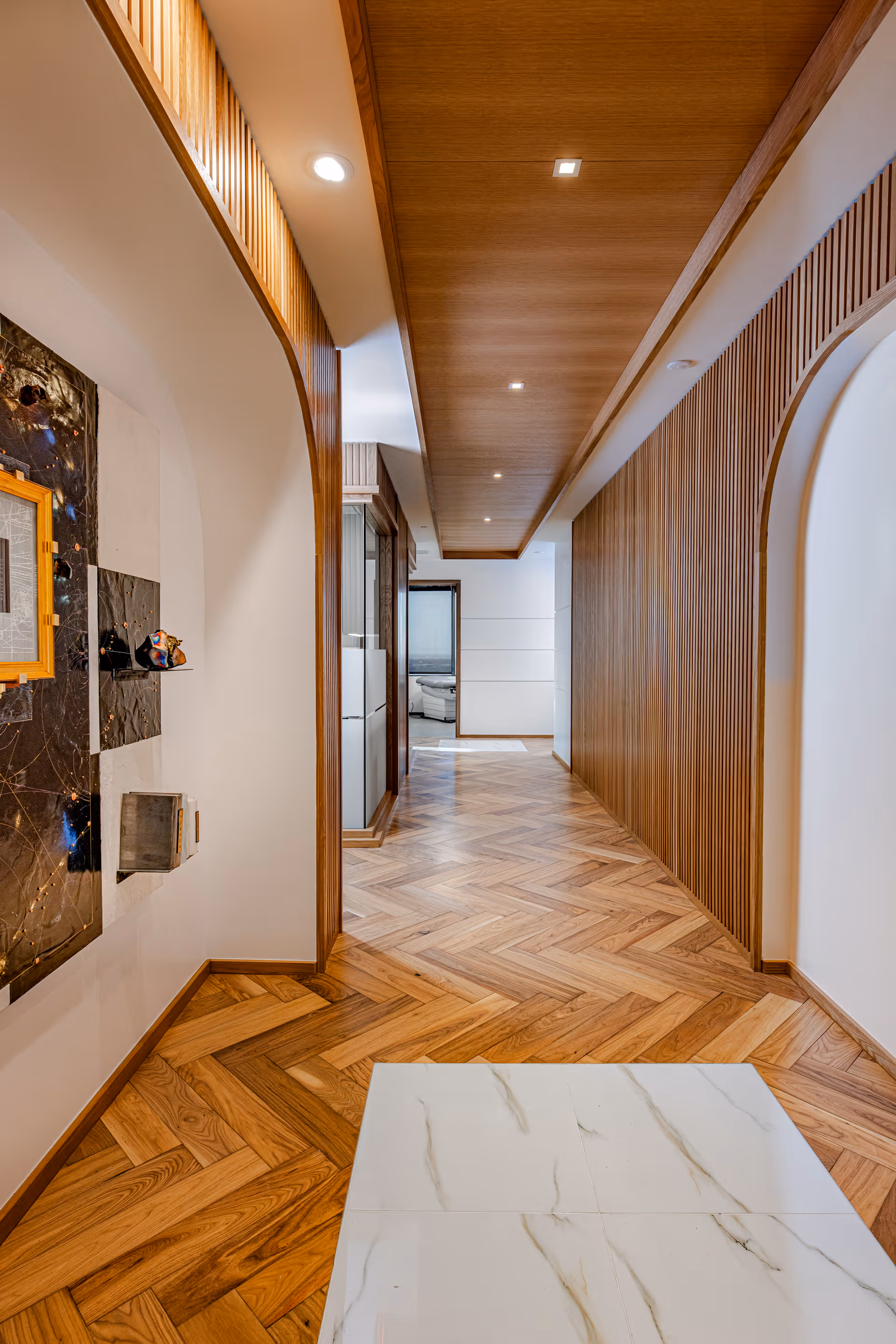 Long interior corridor with wooden-paneled walls, recessed lighting, and herringbone wood floor.
