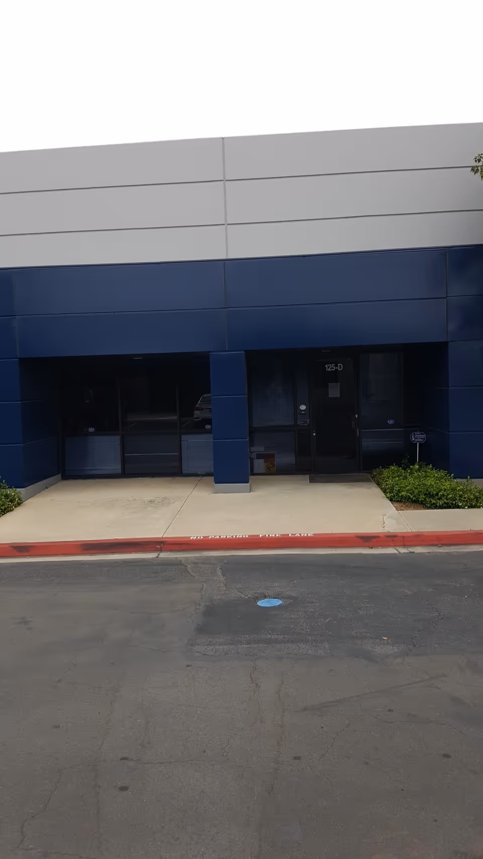 Blue storefront entrance with glass doors and a sidewalk in front of a facility.