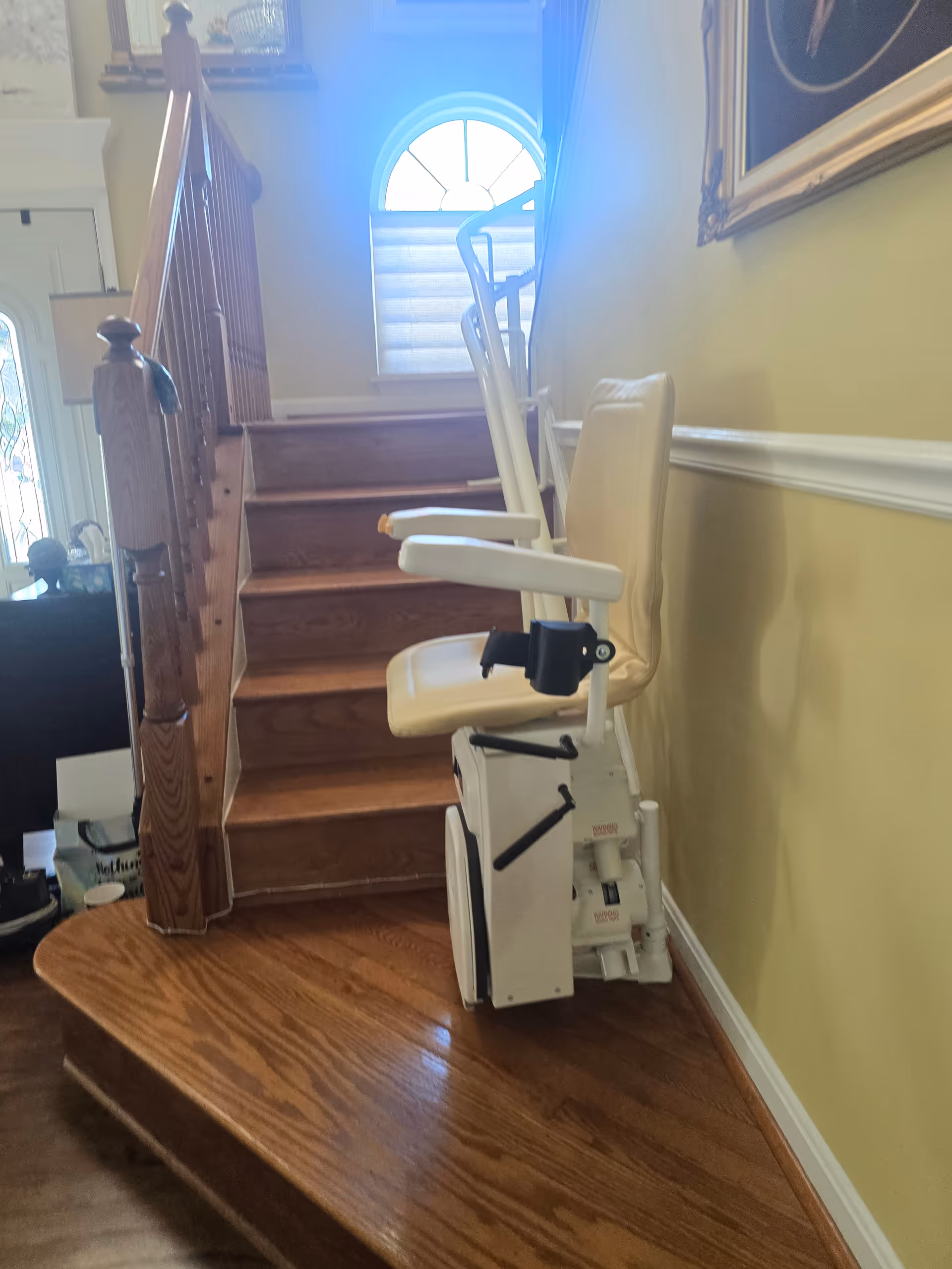 Indoor staircase with a beige stairlift chair attached to wooden steps and yellow walls