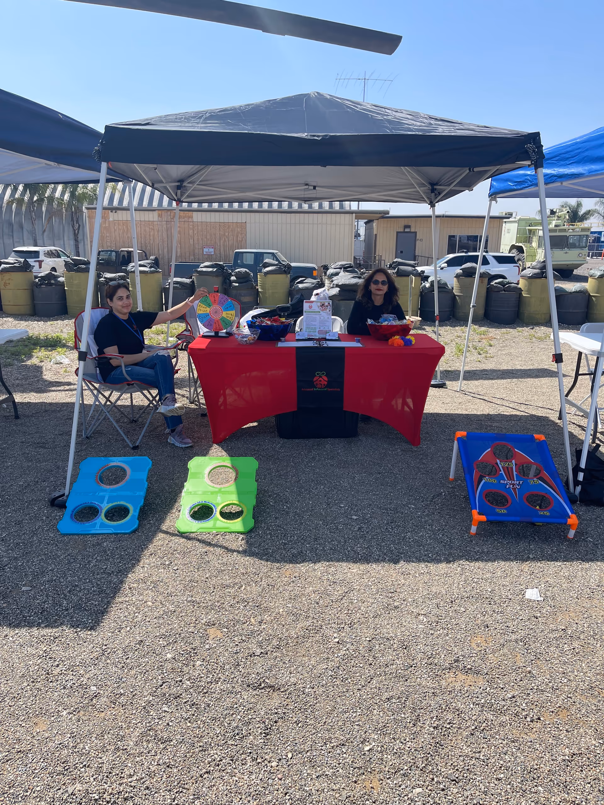 Two volunteers host an outdoor booth under a canopy with games on a sunny day.
