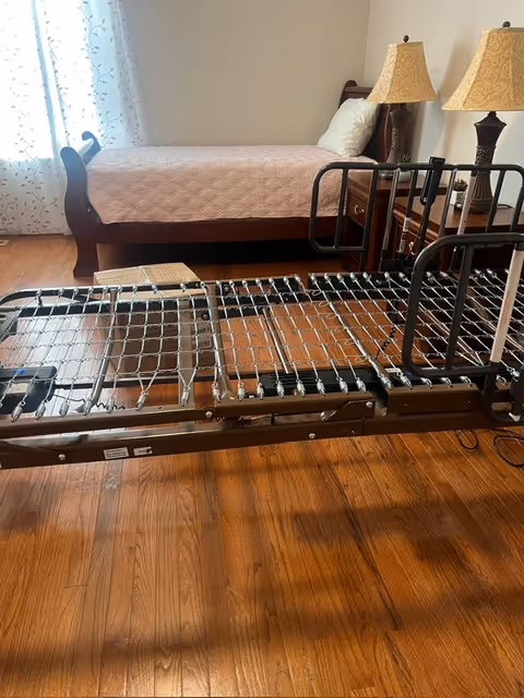 An adjustable hospital bed frame with rails in a furnished bedroom.
