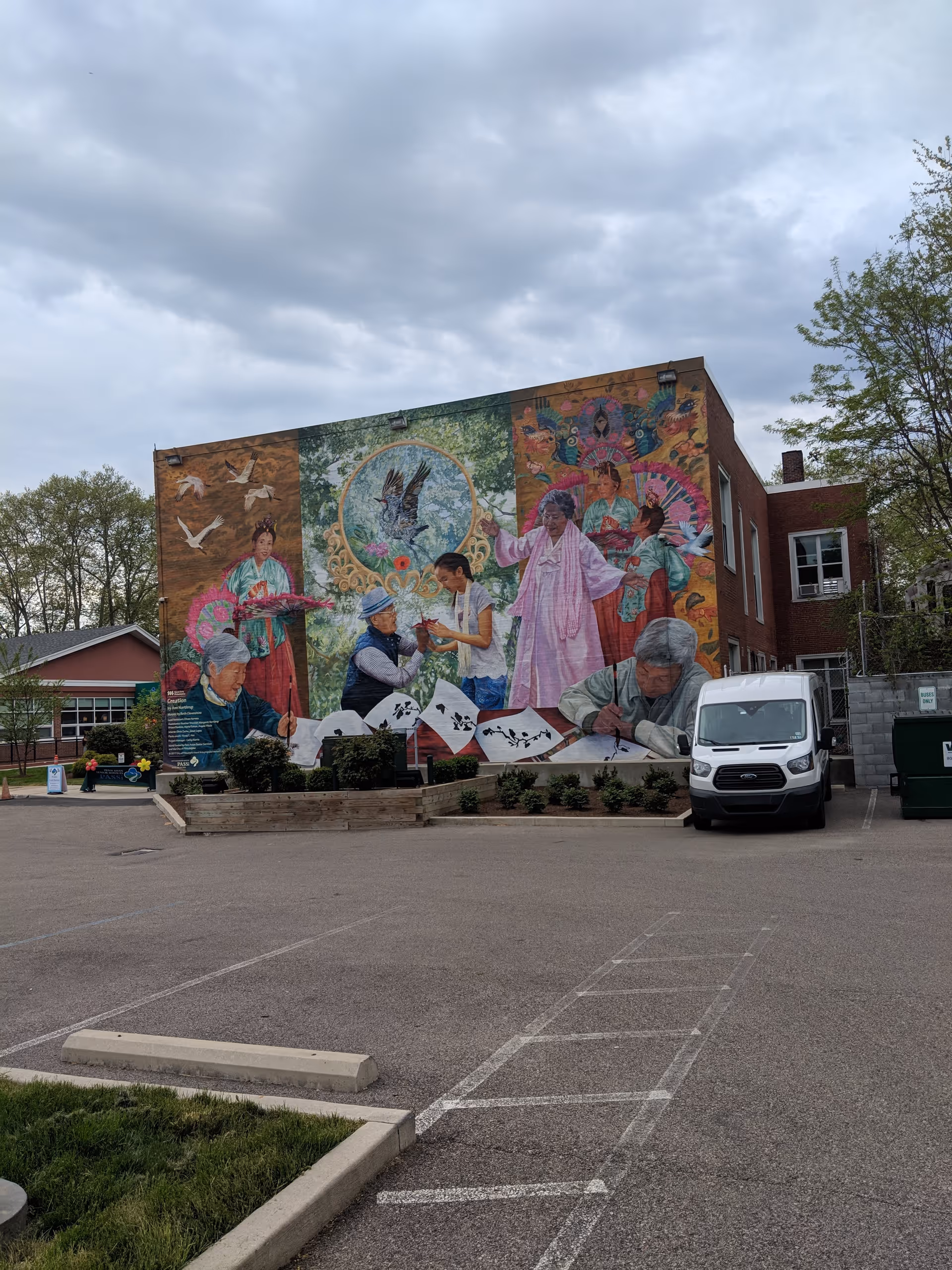 Exterior brick building with vibrant mural and a white van in a parking lot.