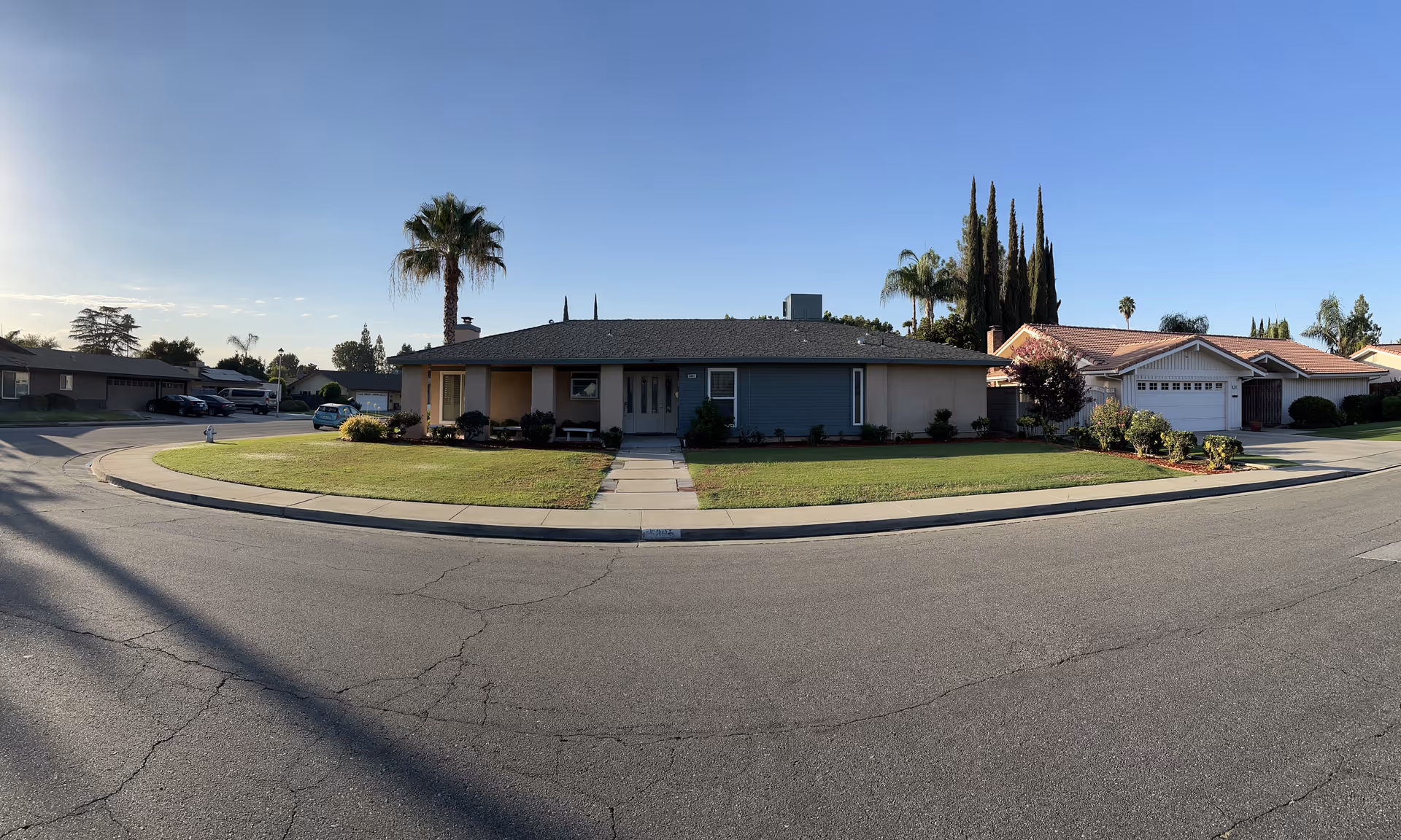 Wide view of a single-story house on a curved street with a manicured lawn.