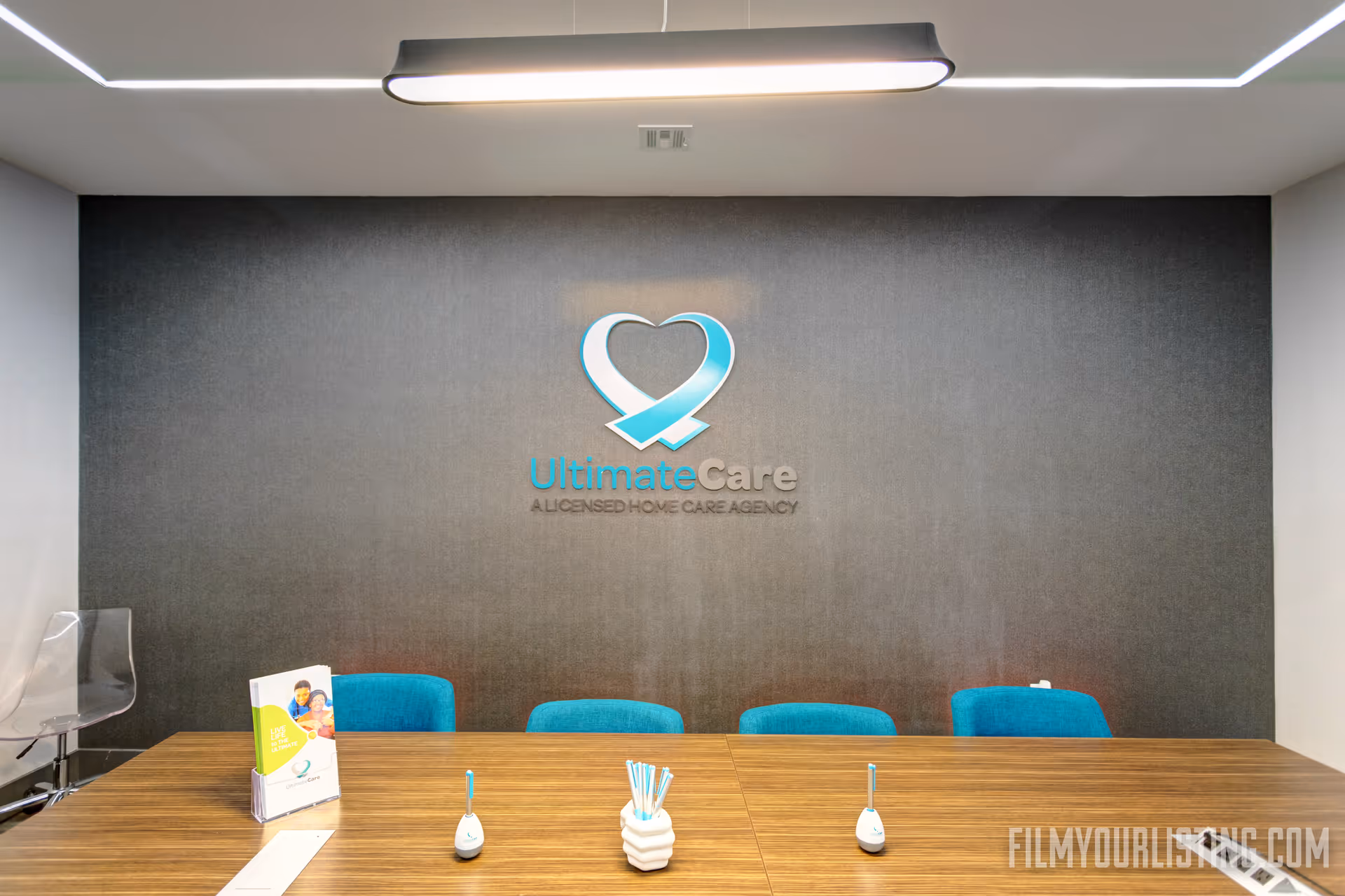 Reception area with a wooden table, blue chairs, and the UltimateCare logo on a dark wall.