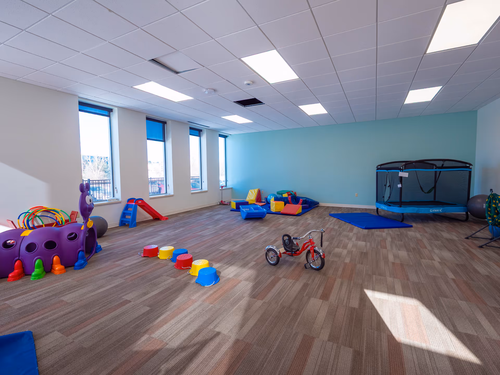 Colorful children's playroom with trampolines, soft blocks, and a tricycle in a bright room.
