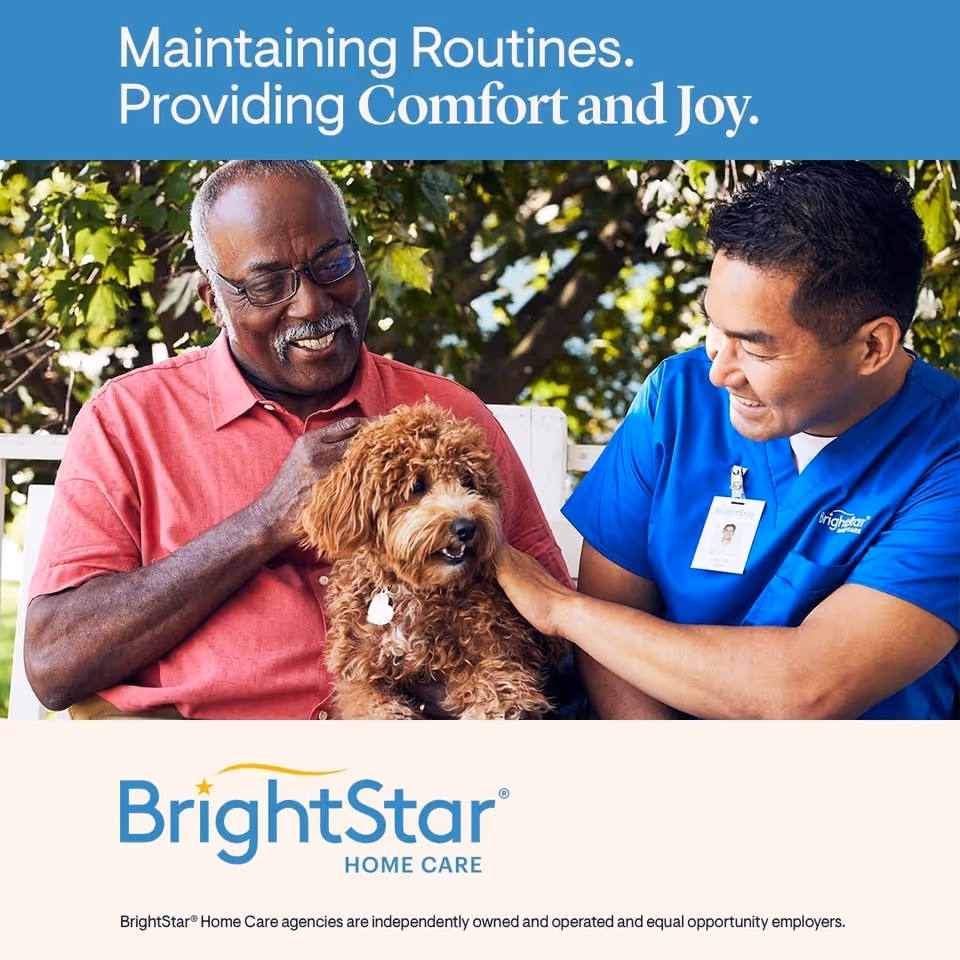 Elderly man outdoors with caregiver smiling while petting a small brown dog.