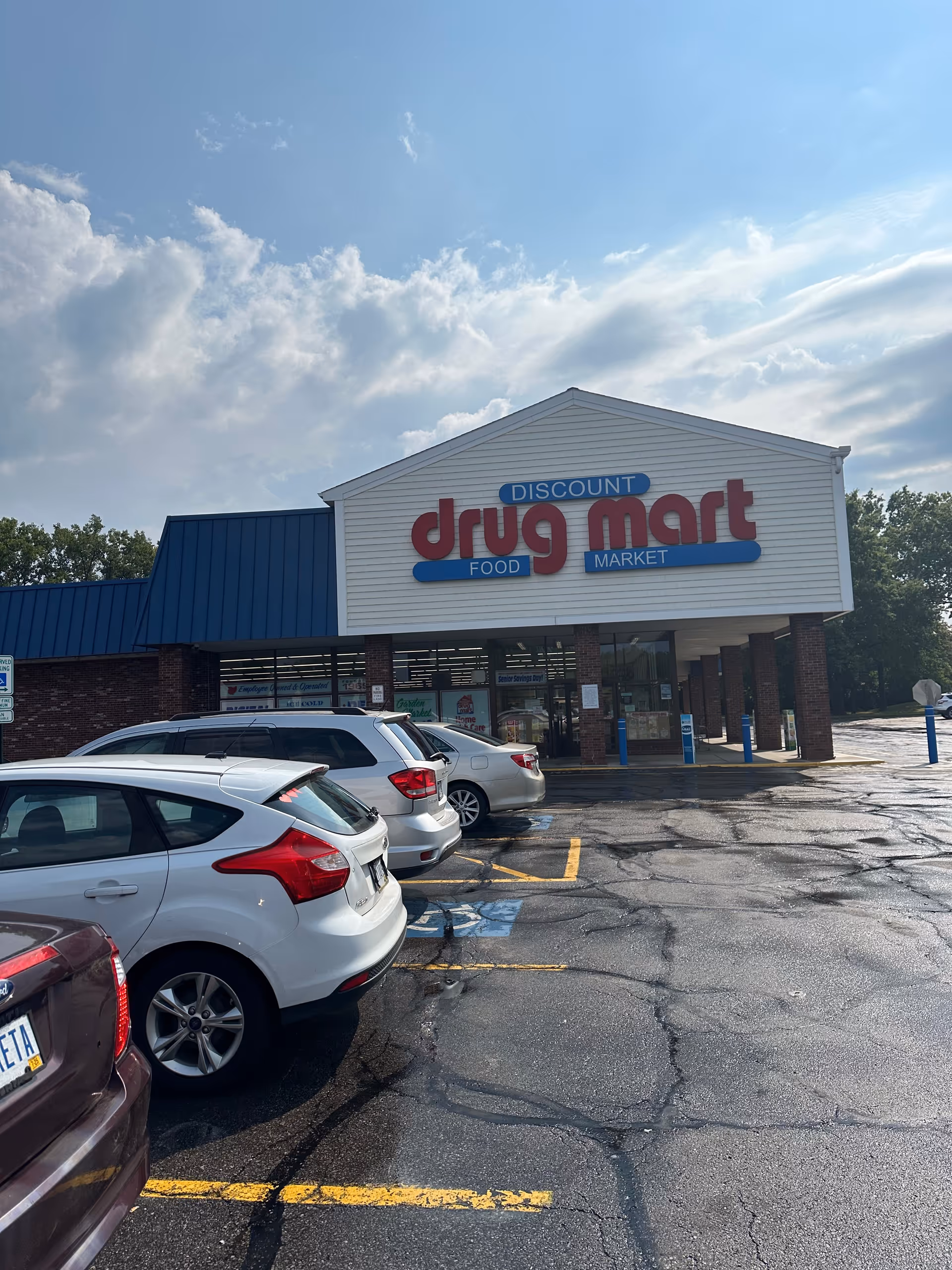 Discount Drug Mart storefront with sign, white building, blue awning, brick columns, and parked cars.