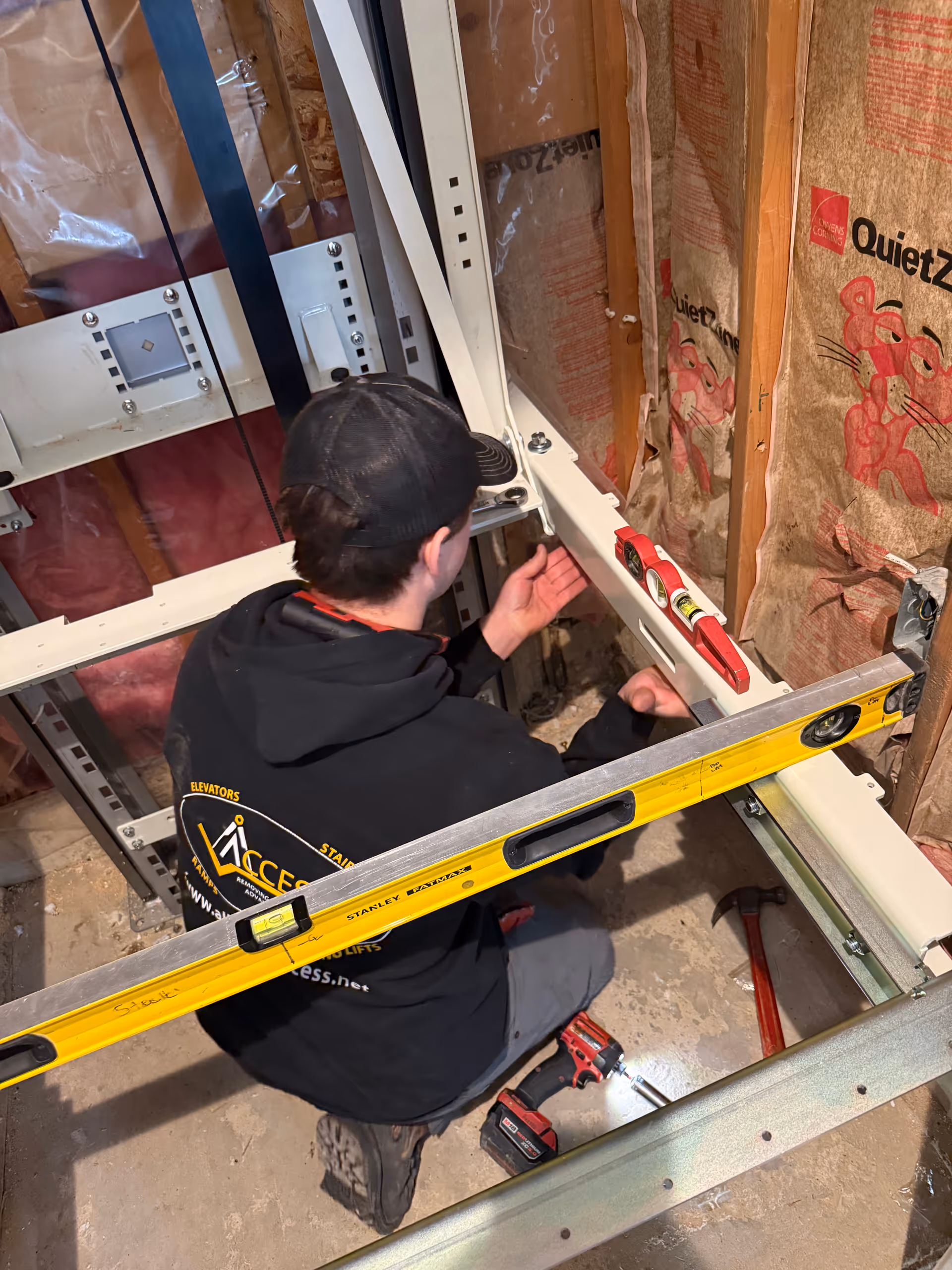 Worker from Access Elevator, Inc. installs elevator components inside a partially finished interior.