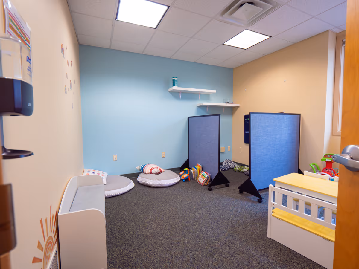 Interior playroom with blue walls, cushions, a crib, books, and blue dividing screens.