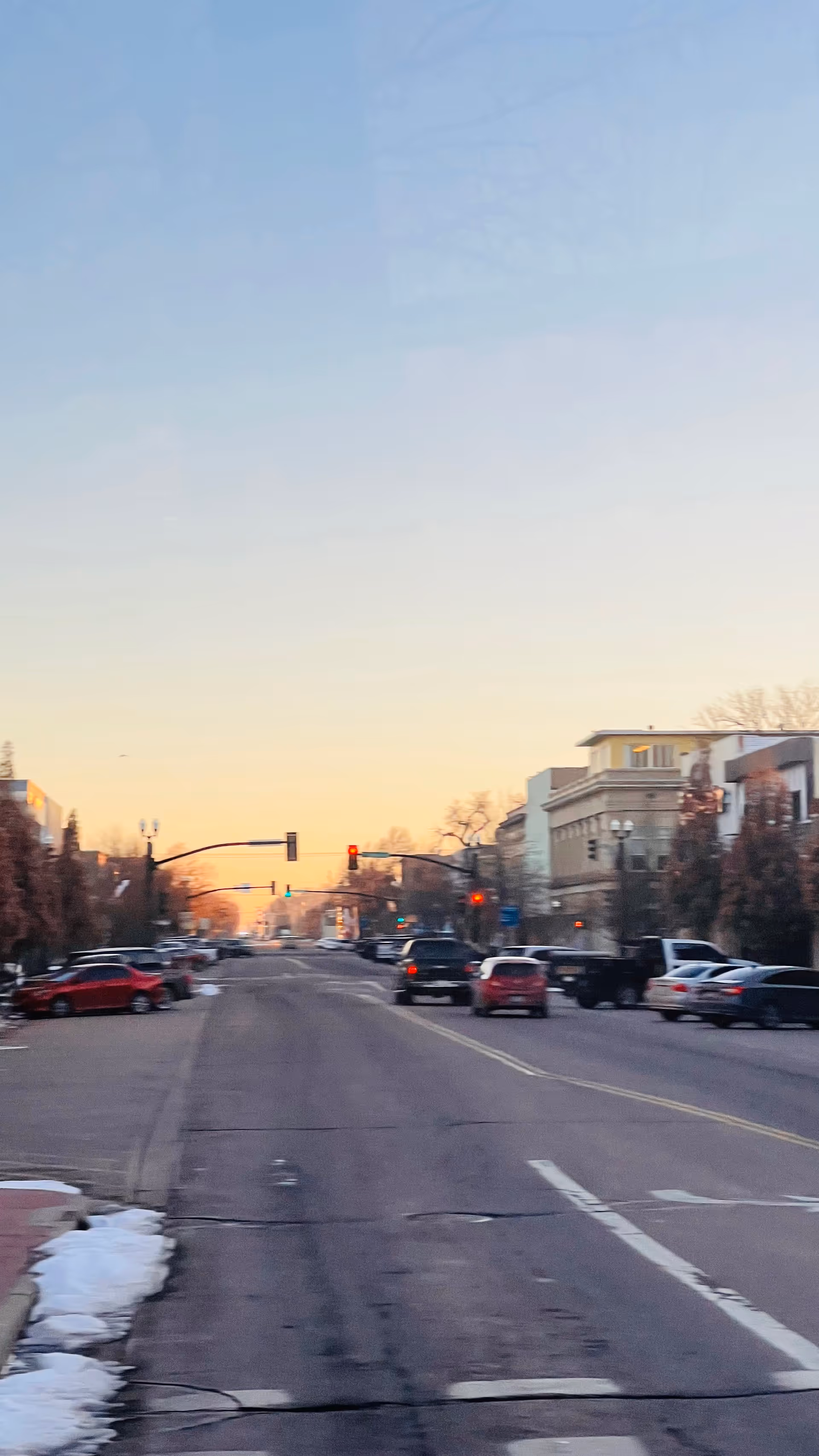 Sunset-lit city street with parked cars and buildings along both sides.