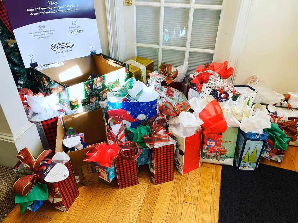 Gift bags and boxes overflow from a box near a window in a Home Instead entryway.
