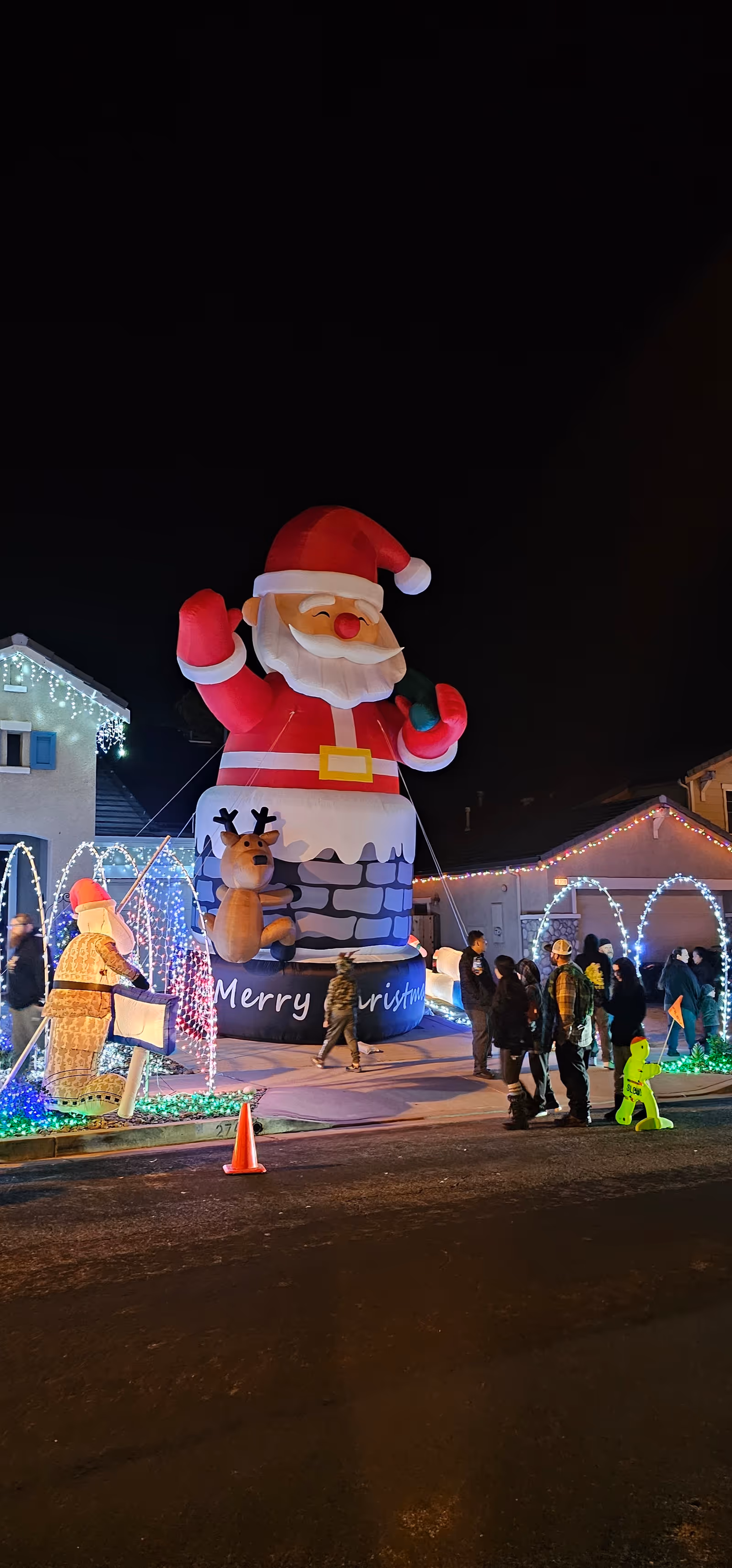 Nighttime outdoor holiday display with a large Santa inflatable and illuminated arches.