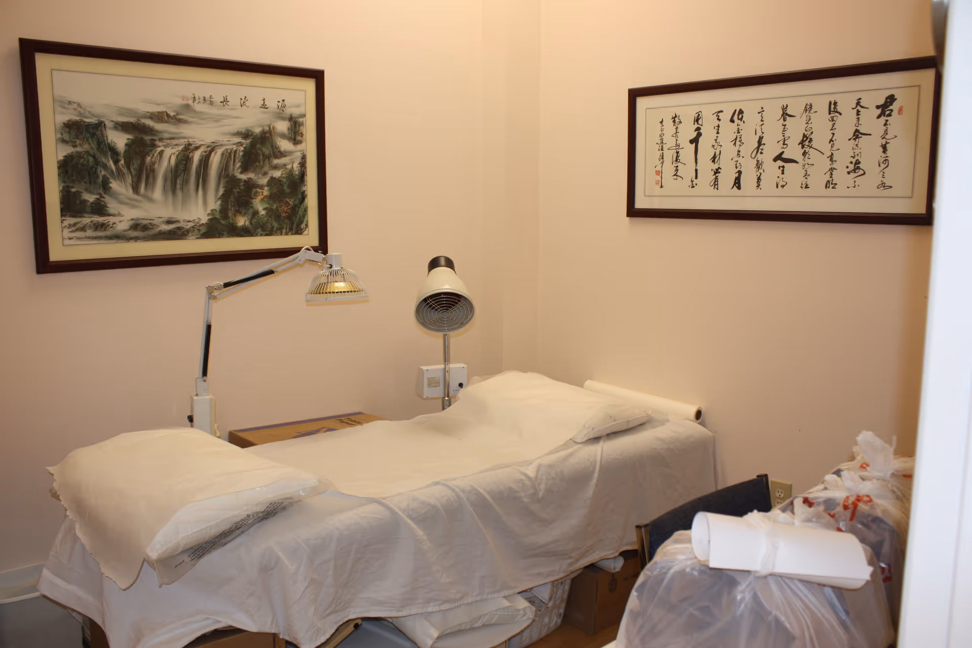 Treatment room featuring a massage table, adjustable lamp, and framed Chinese artwork.