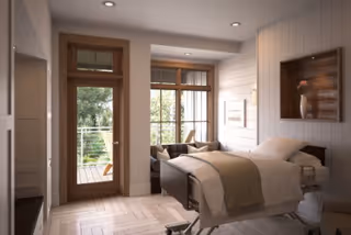 Bright bedroom in a senior facility with a bed, seating, and balcony doors.