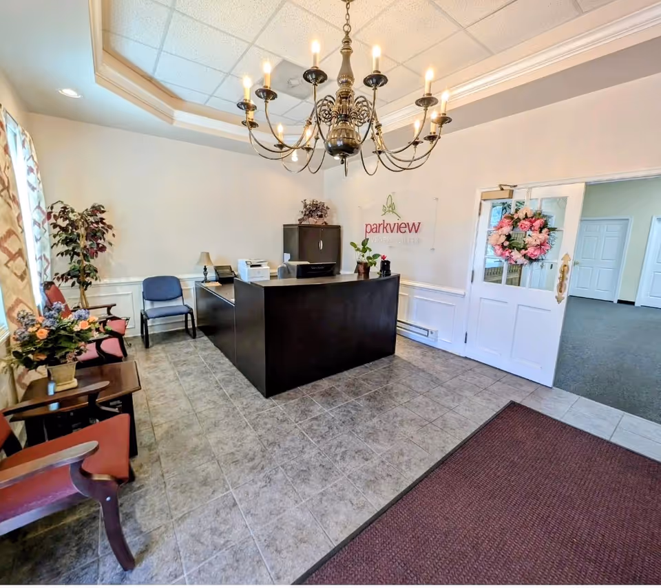 Reception lobby with a dark curved desk, chandelier, seating, plants, and doorway to offices.