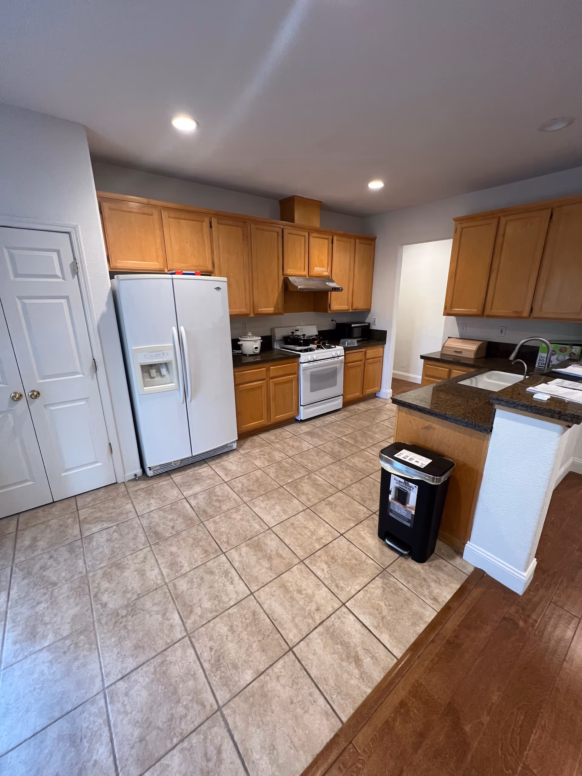 Bright kitchen with wooden cabinets, white appliances, sink, and granite island.
