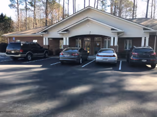 Brick, single-story building with a covered entrance and multiple cars parked in front.