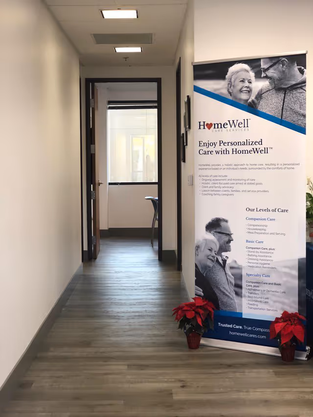Indoor hallway featuring a HomeWell banner and red poinsettia plants.