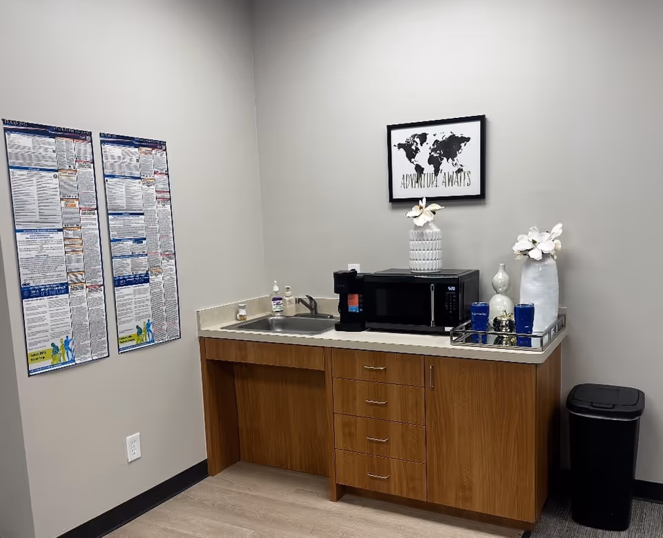 A small staff kitchenette with microwave, sink, coffee maker, posters, and wall art.