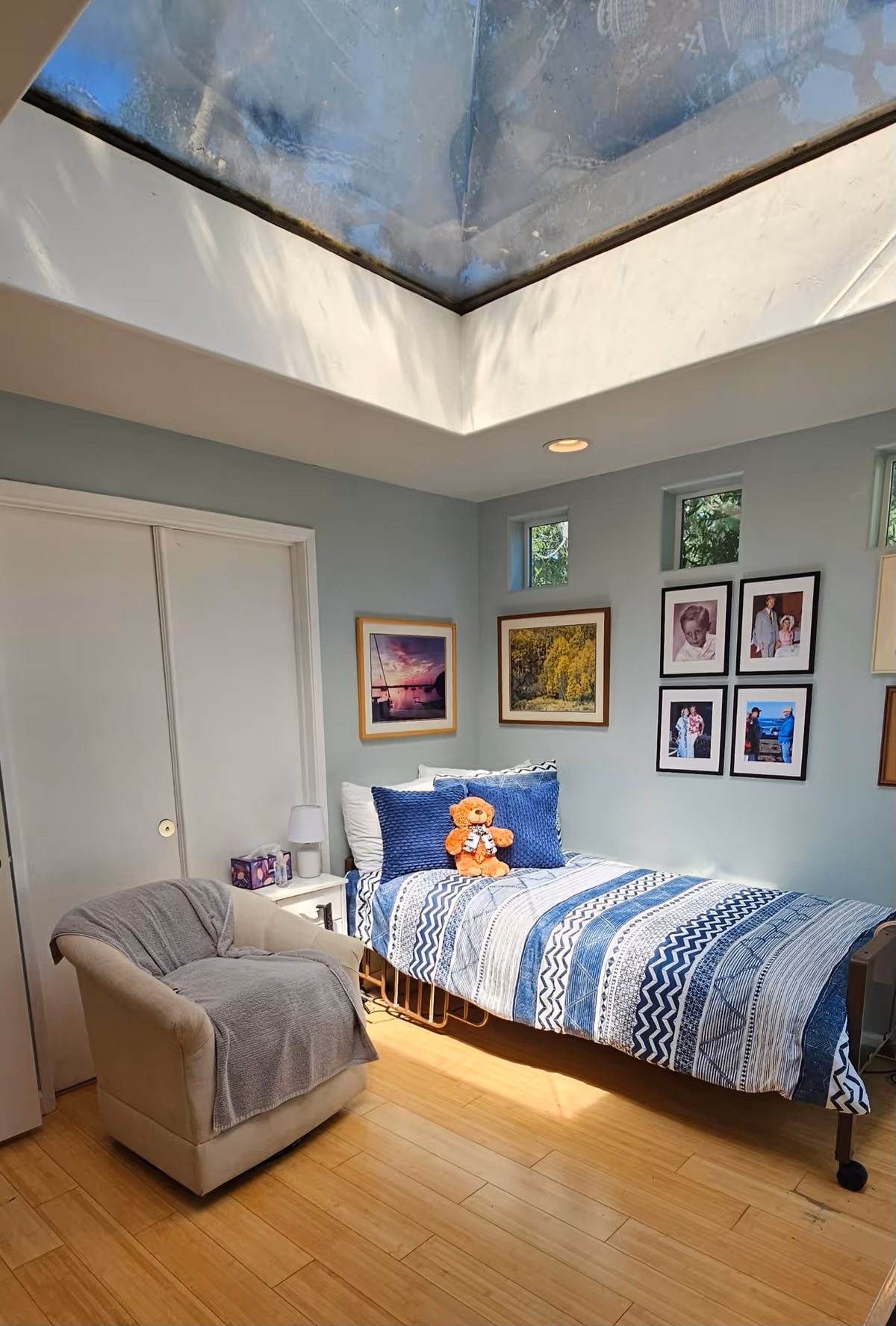 A bright bedroom with a skylit ceiling, single bed, blue striped bedding, and photos.