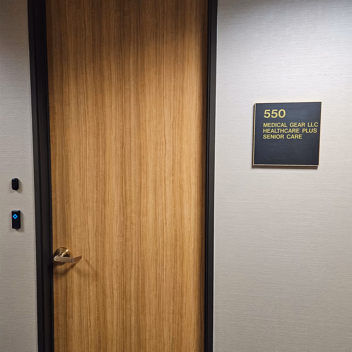 Wooden door with brass handle beside plaque reading '550 Medical Gear LLC Healthcare Plus Senior Care'.