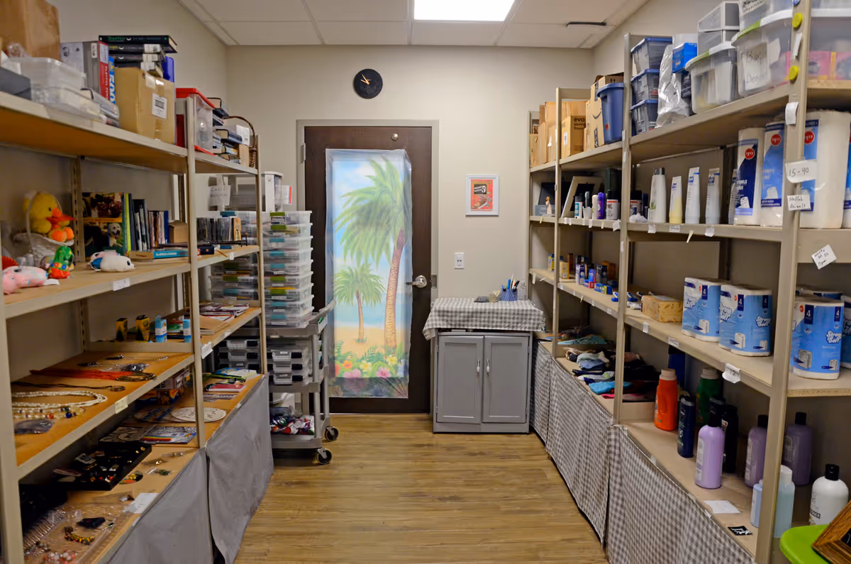 Narrow storage room with shelves full of supplies and a door featuring a palm tree mural.