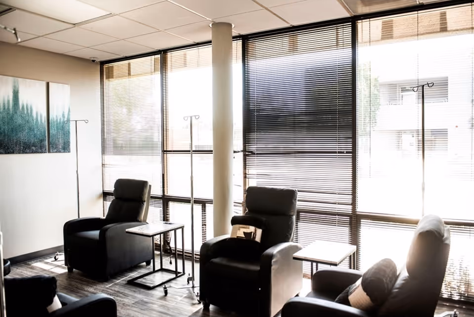 Bright interior waiting area with recliner chairs, IV pole stands, and large blinds.