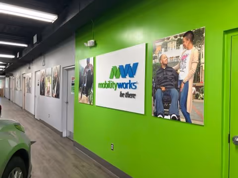 A bright green hallway with MobilityWorks signage and mounted photos along a modern interior corridor.