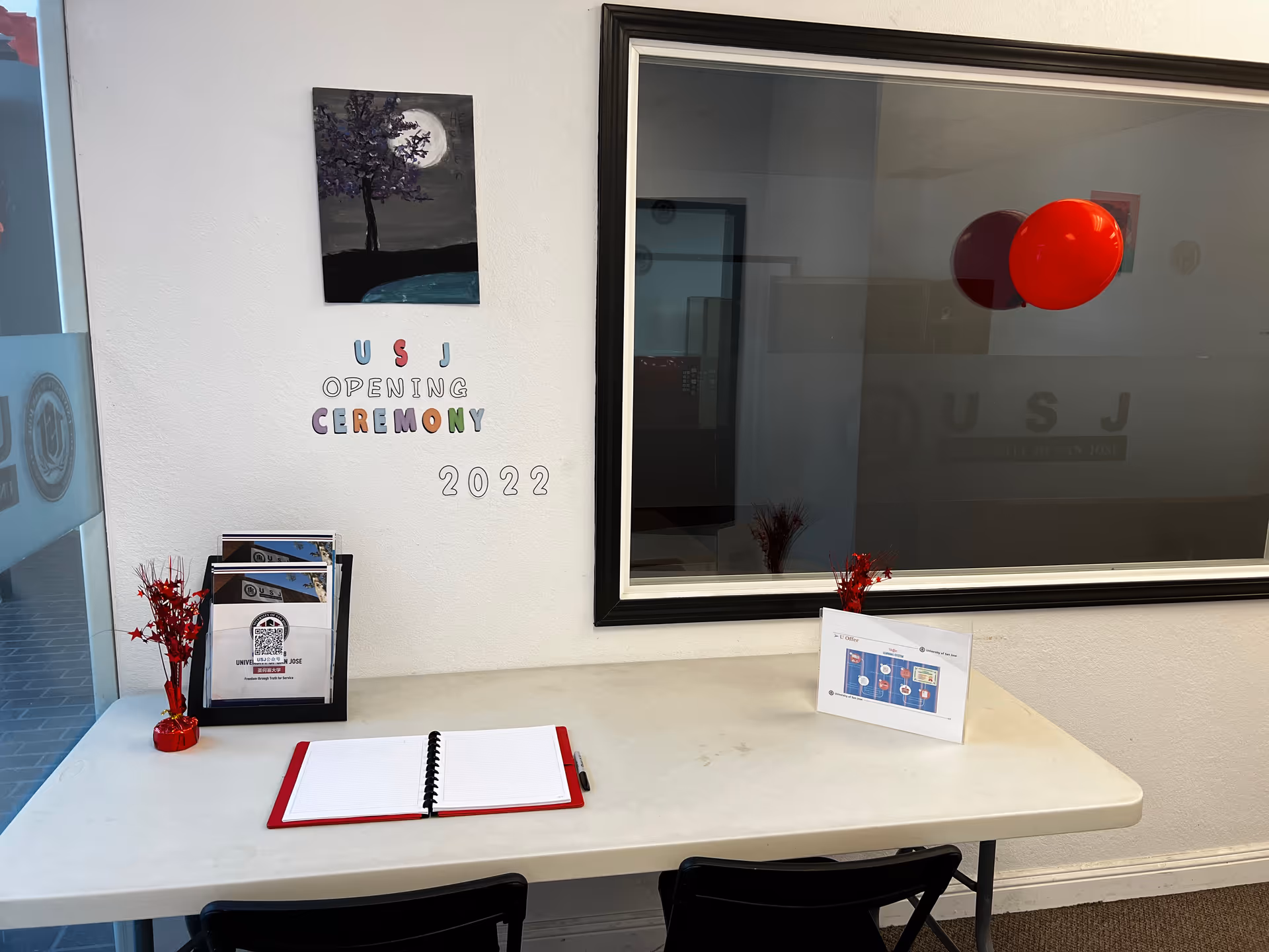 Interior desk area with a notebook, brochures, and a wall noting USJ opening ceremony.