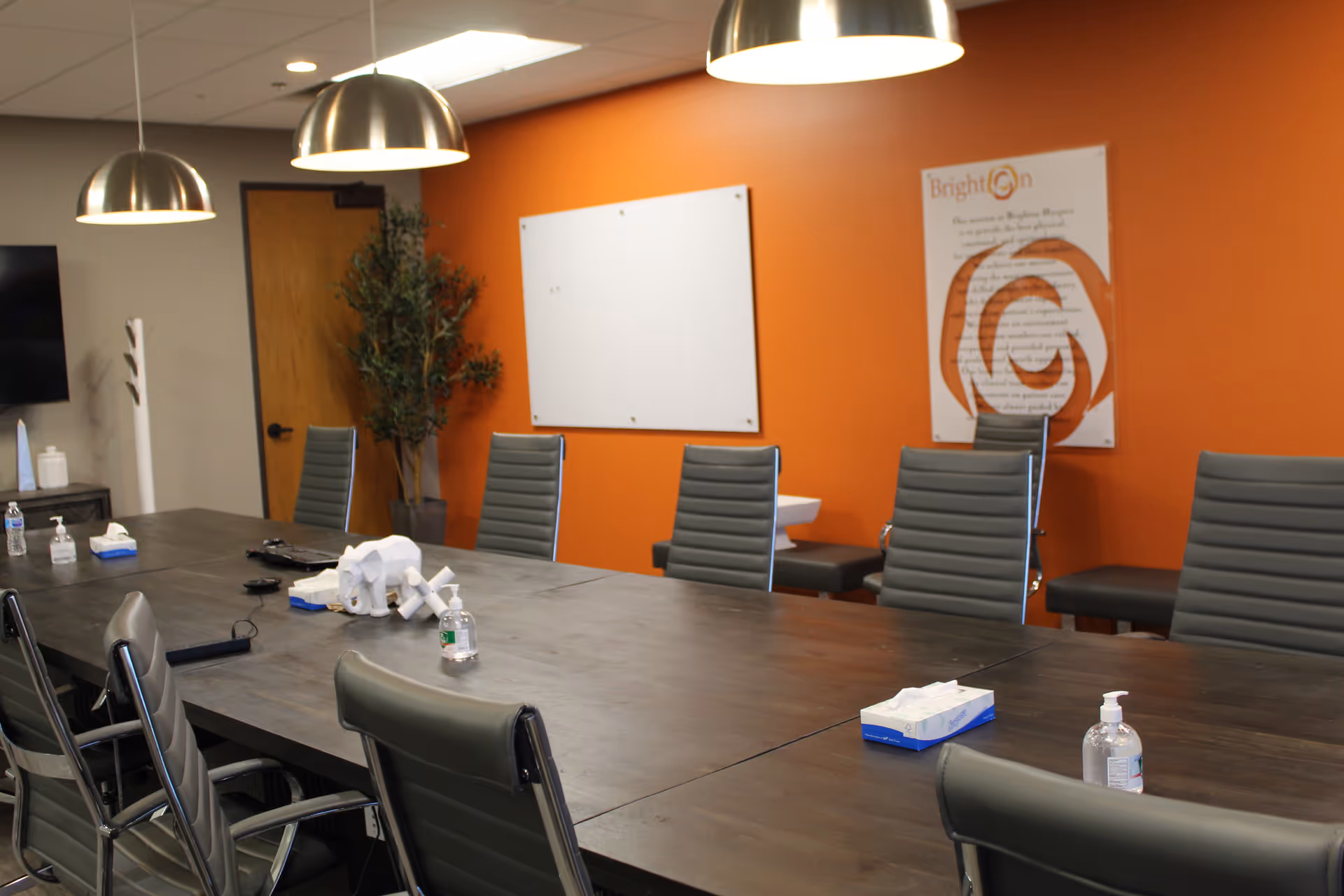 A long conference table with chairs in a bright orange-walled meeting room.